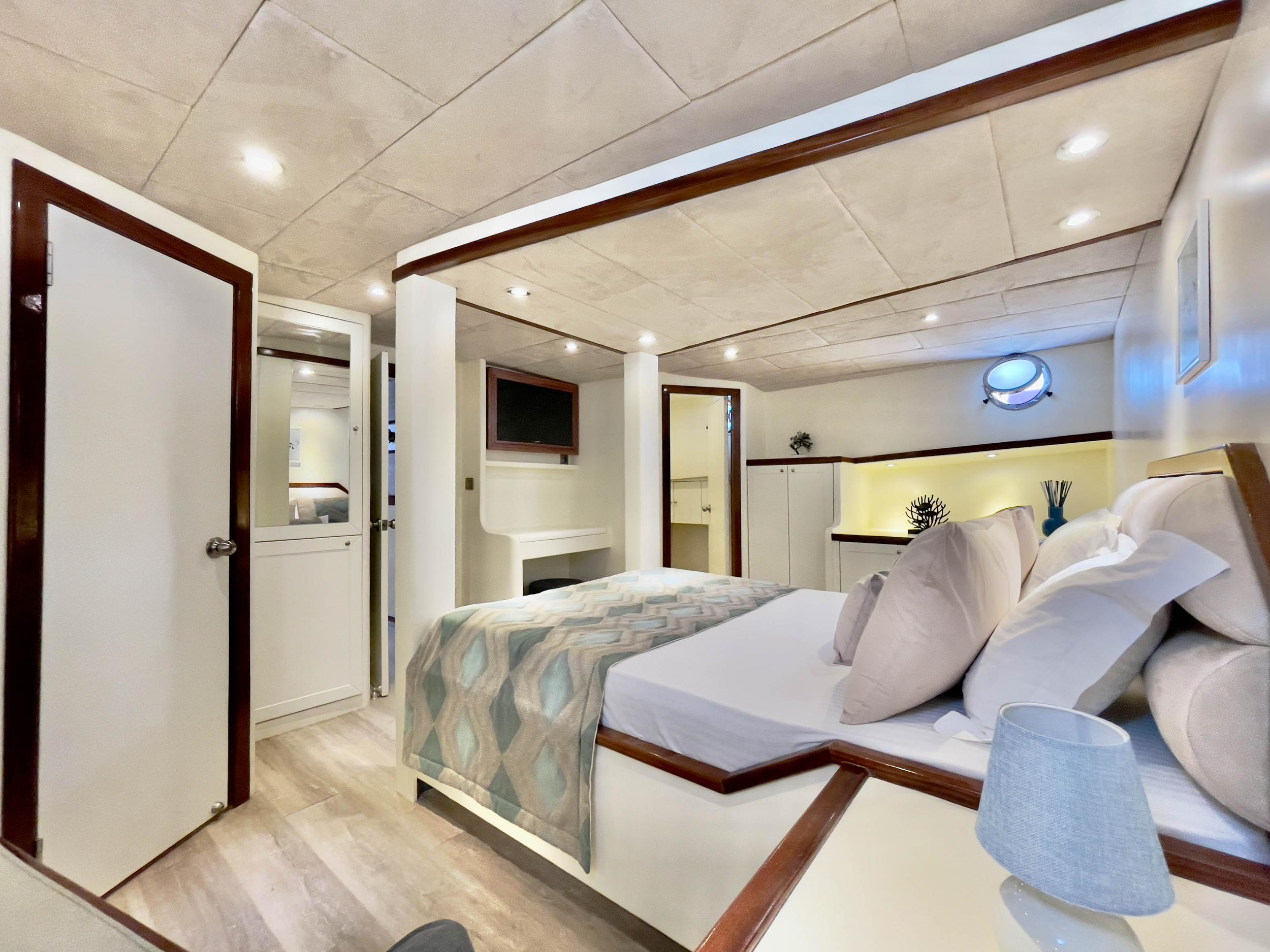 Spacious master cabin with king bed, flat-screen TV, walnut trim, and en-suite doorways