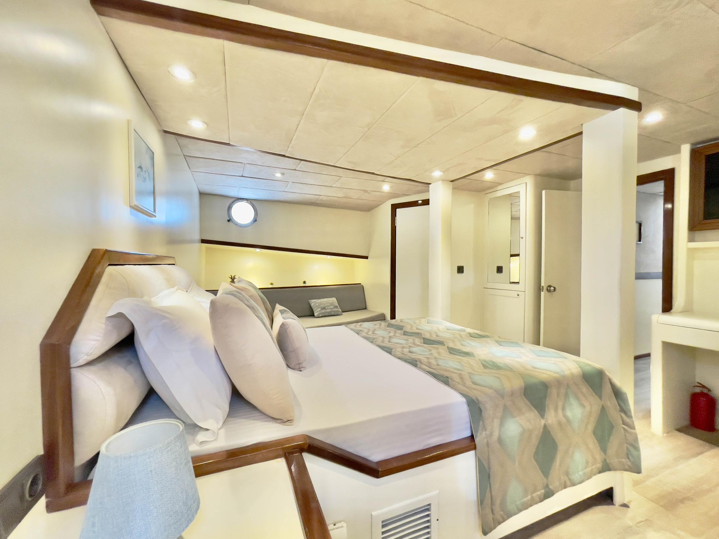 Spacious double cabin with king bed, geometric throw, wooden headboard, porthole window, and en-suite door