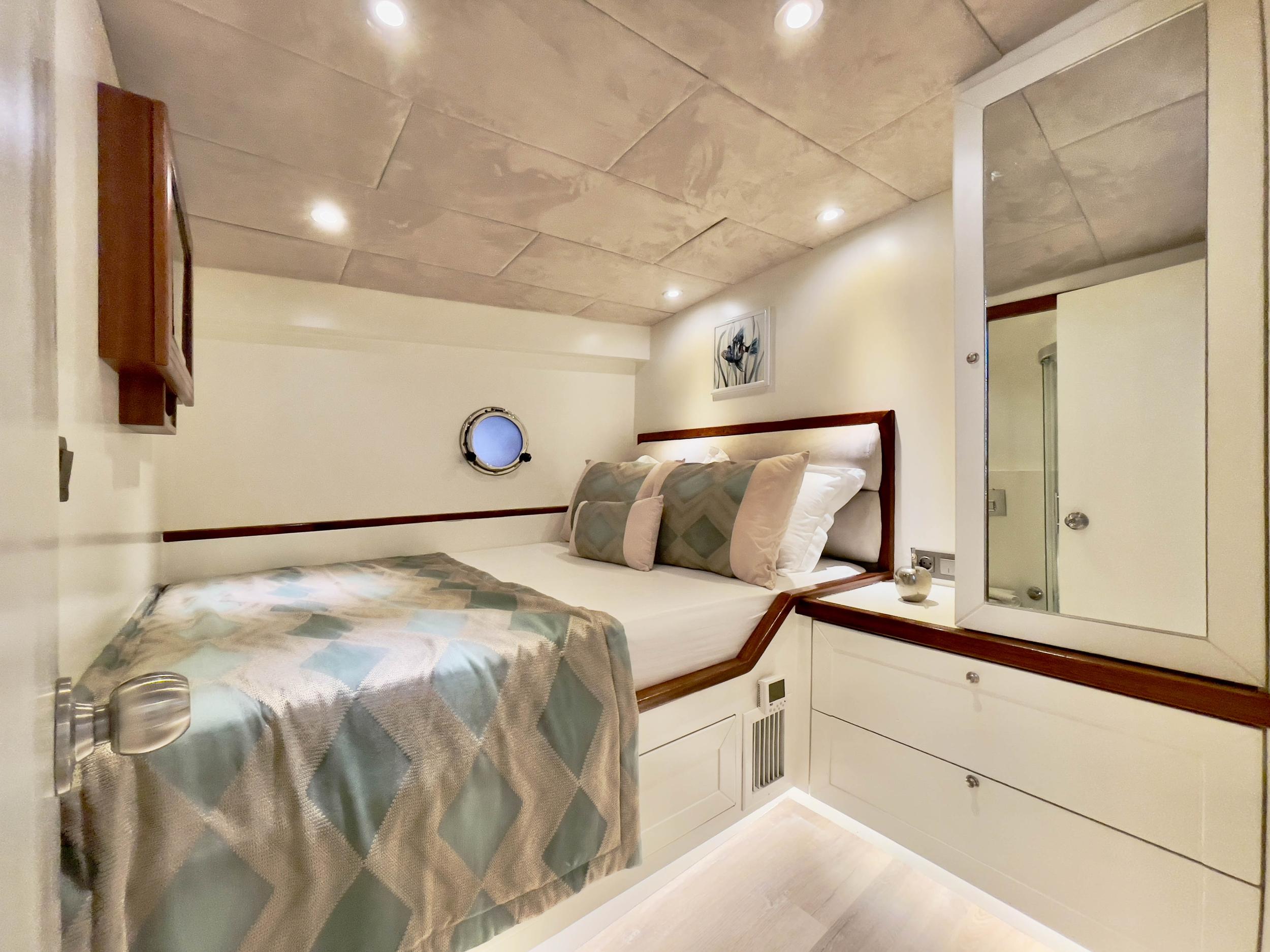 Yacht double cabin with teak-framed bed, porthole window, recessed lighting and en-suite entrance