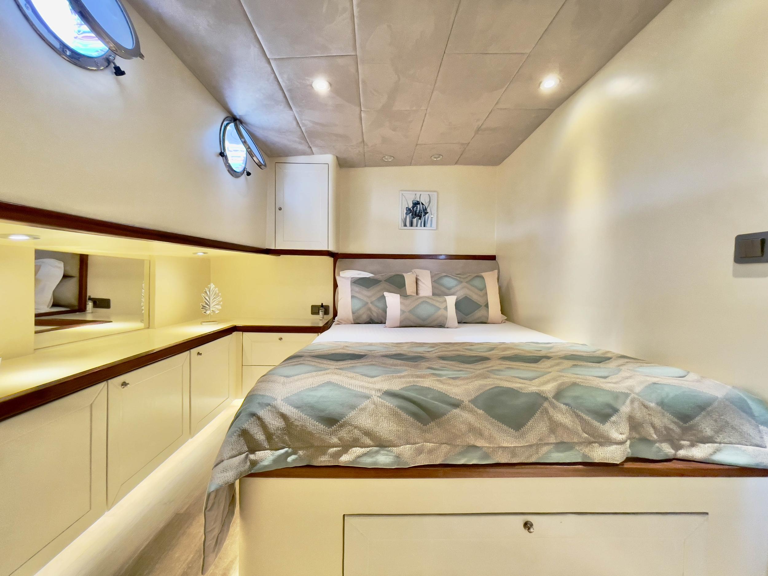 Gulet double cabin with diamond-patterned bedding, built-in cream cabinetry, and two round porthole windows