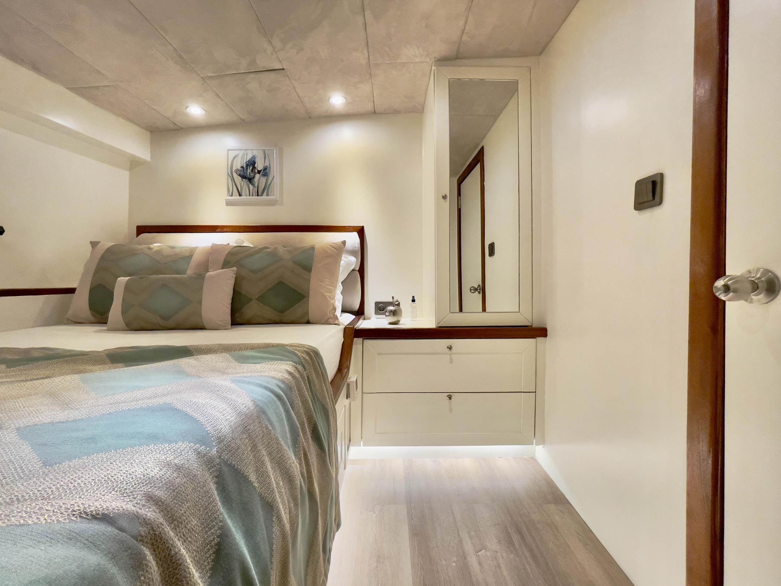 Yacht double cabin with teak headboard, sage green cushions, built-in drawers, and full-length mirror