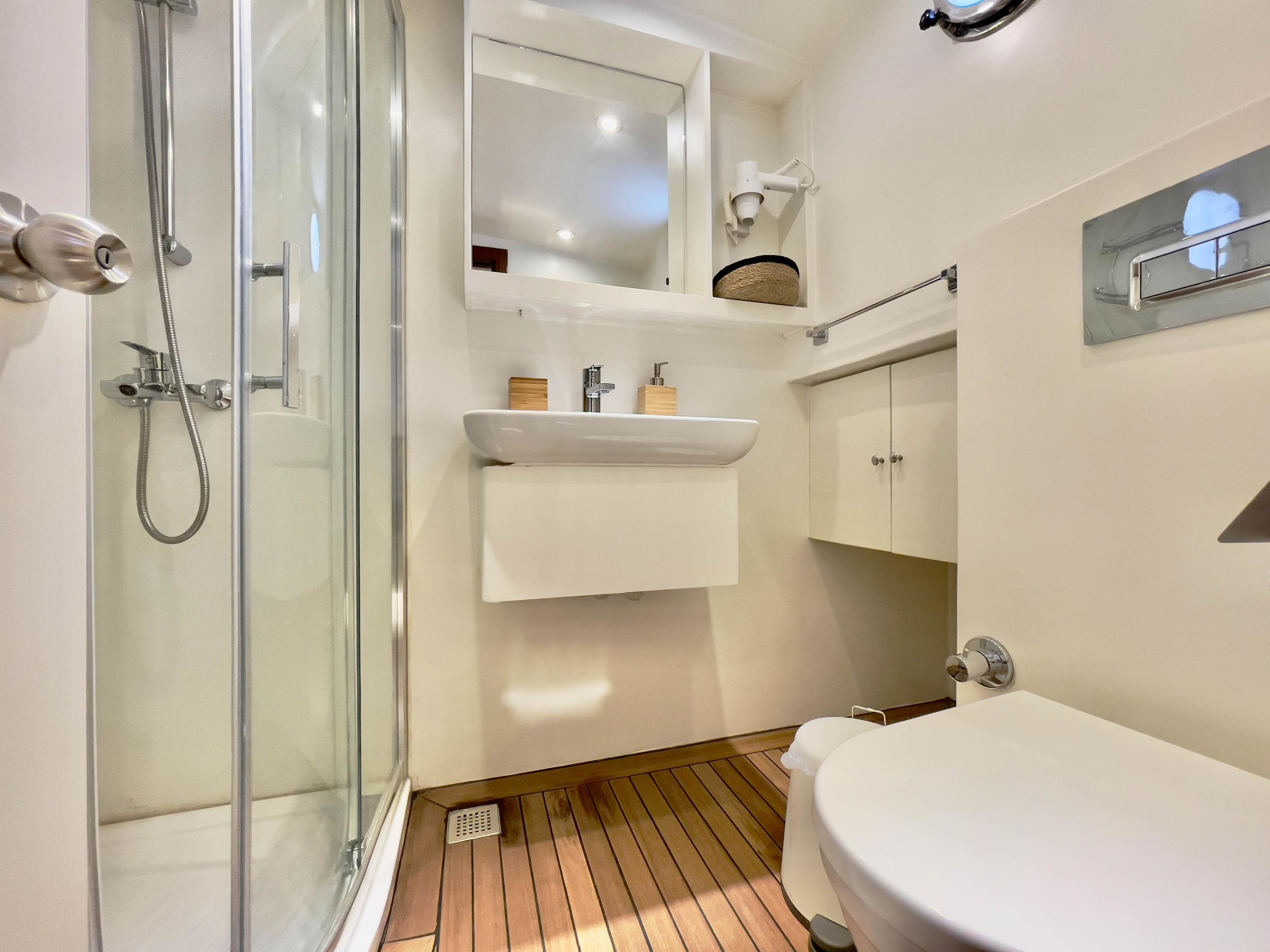 Yacht en-suite bathroom with curved glass shower cubicle, wall-mounted basin, teak slatted floor and marine toilet