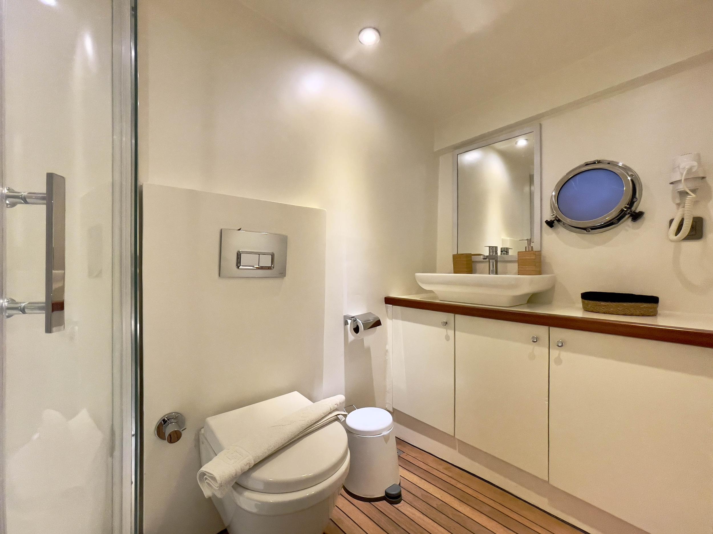 Yacht en-suite bathroom with glass shower, vessel porthole, vessel basin on teak vanity unit and teak floor