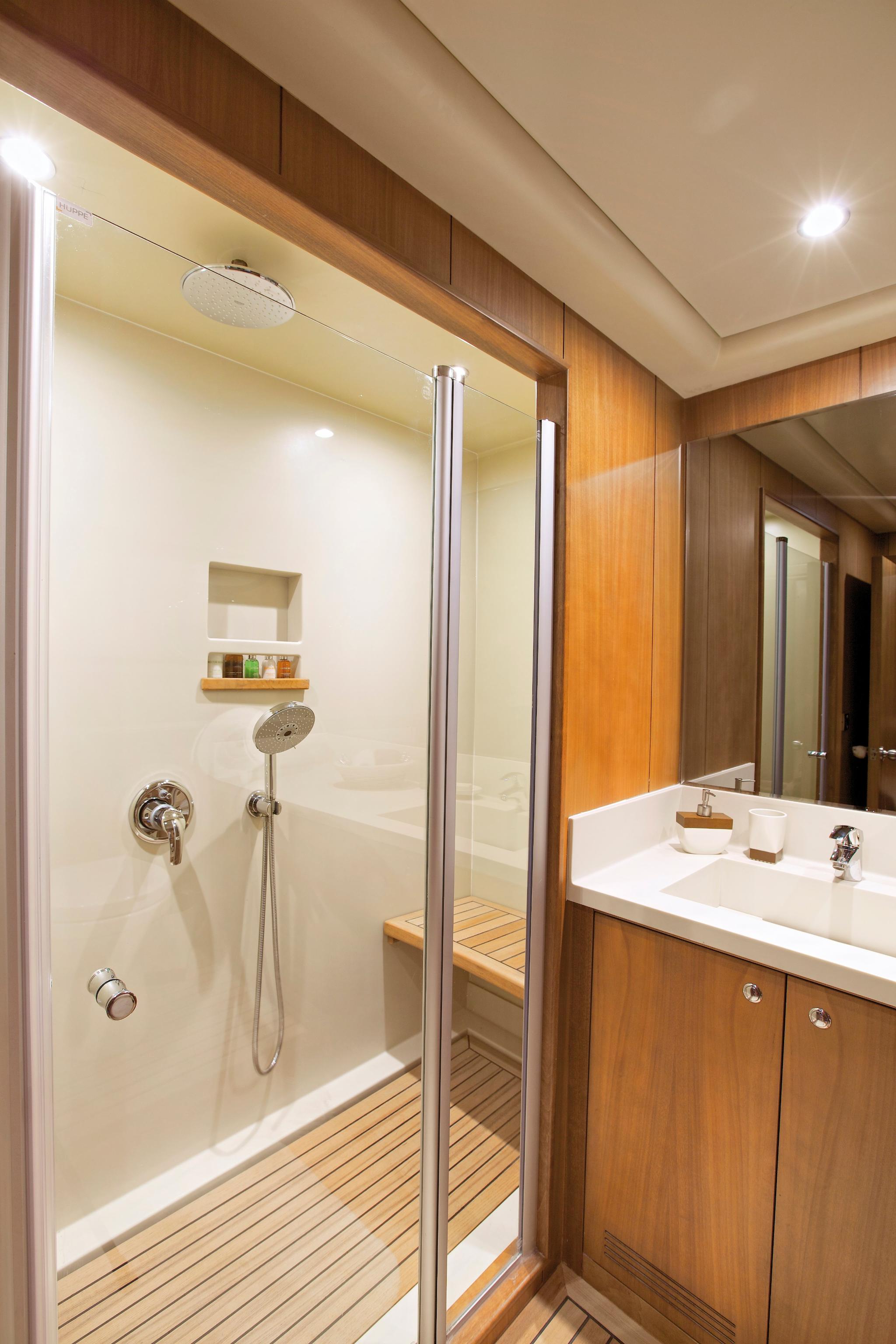luxury yacht bathroom with glass shower enclosure, white vanity sink and teak wood flooring