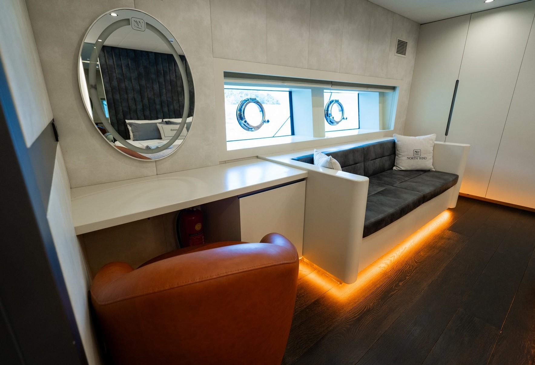yacht cabin interior with white seating area, orange ottoman, circular mirror and twin portholes