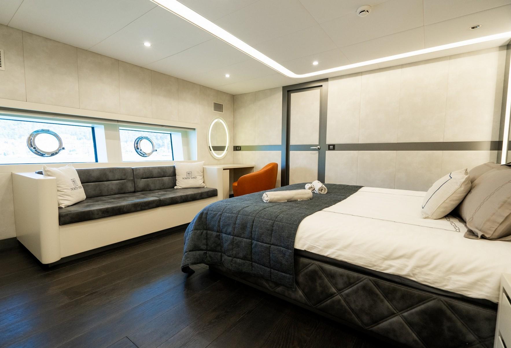 yacht guest cabin featuring double bed with white linens, built-in sofa seating, and porthole windows