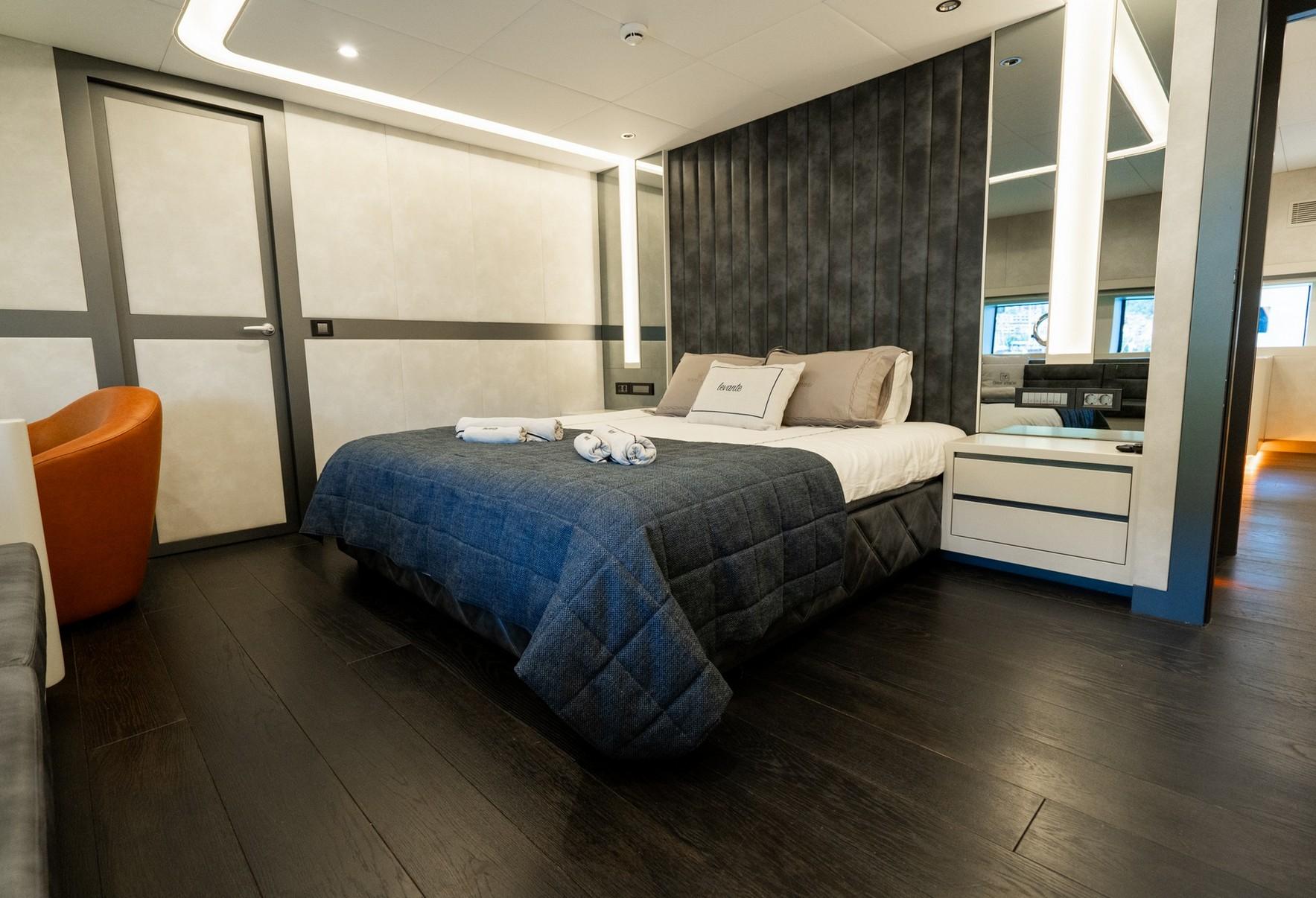 yacht guest cabin featuring double bed with blue bedding, vertical tufted headboard, orange accent chair and built-in storage