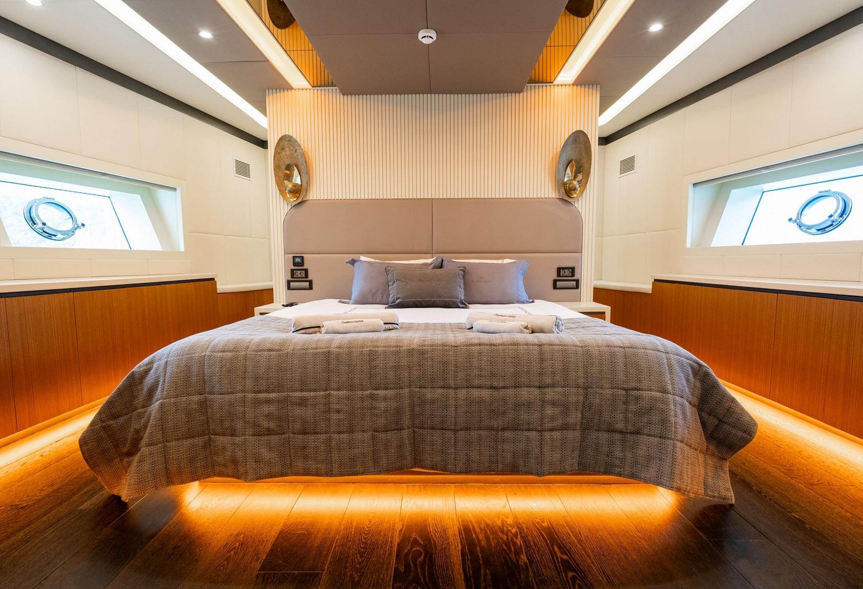 luxury yacht master cabin featuring king bed, vertical wood paneling, twin portholes and ambient lighting