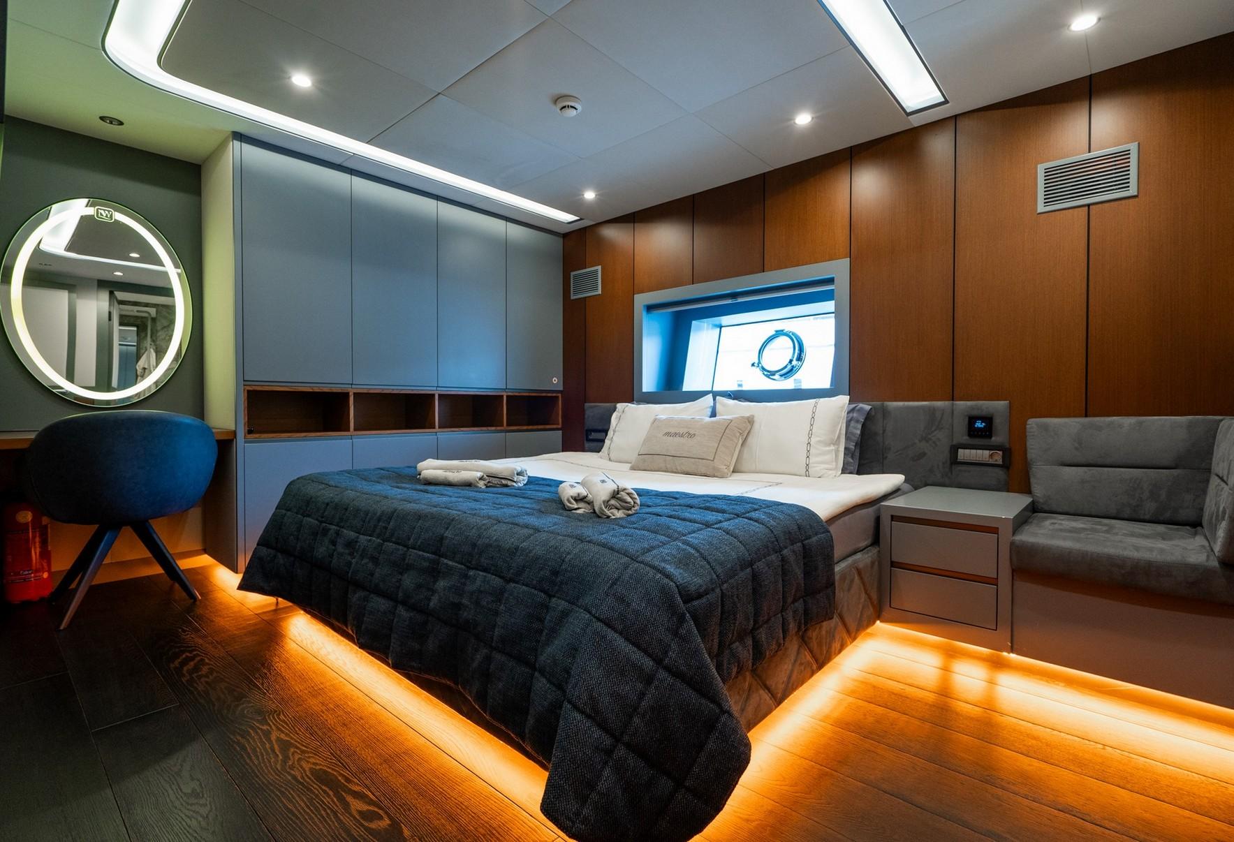 Master cabin with king bed, gray quilted bedspread, built-in seating and porthole window