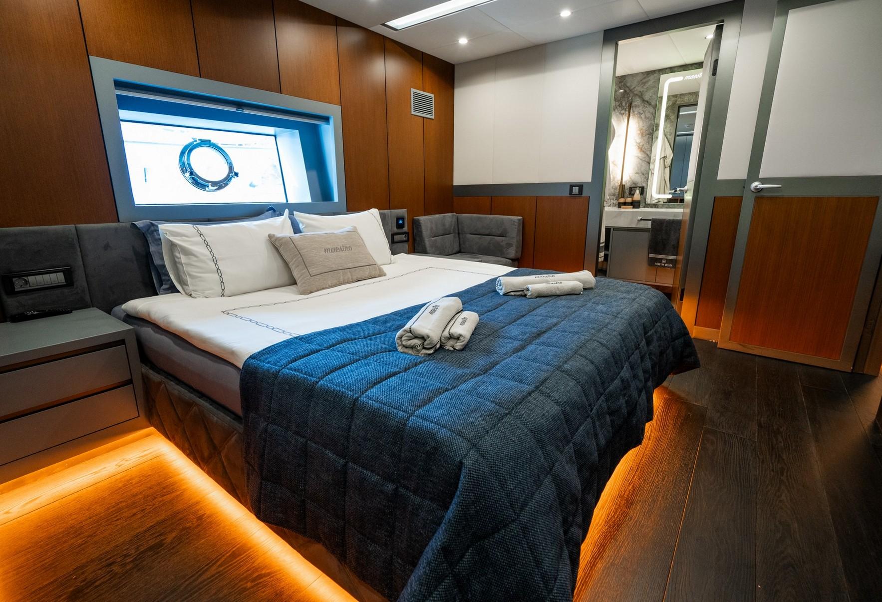 yacht cabin with double bed, blue bedding, porthole window and en-suite bathroom entrance