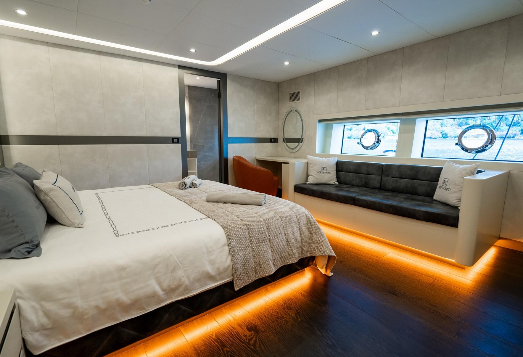 yacht guest cabin featuring double bed with under-bed lighting and built-in seating bench with portholes
