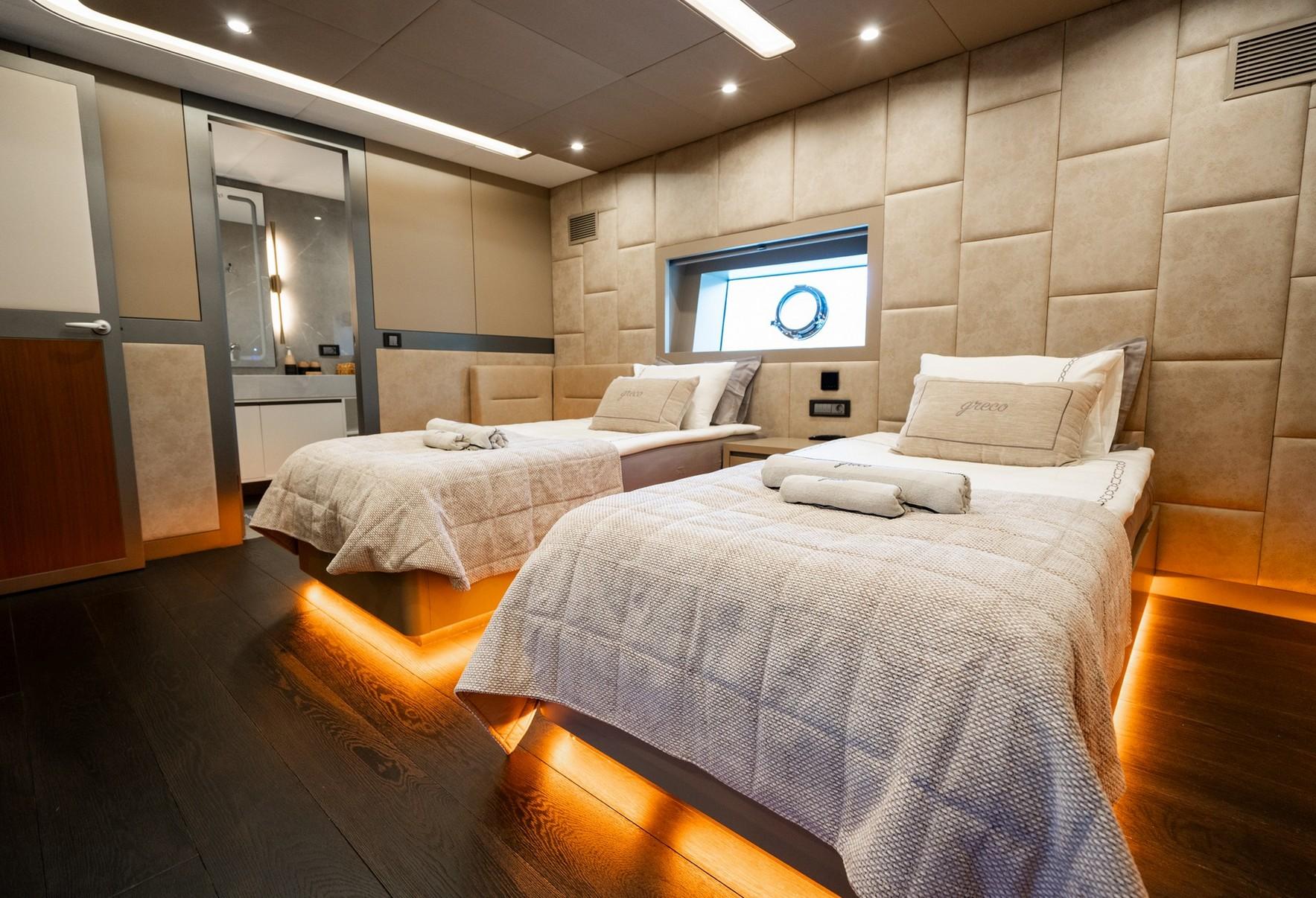 luxury yacht twin cabin with two single beds, beige upholstered walls and ensuite bathroom