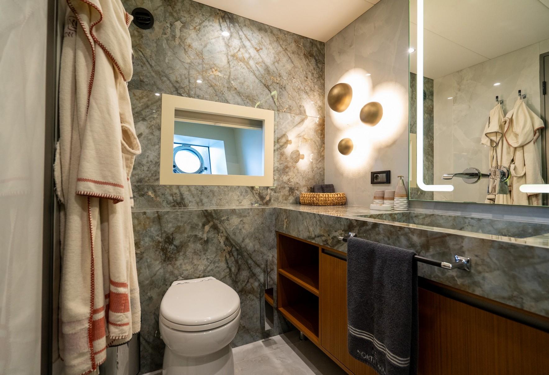 Modern yacht bathroom featuring marble walls, vessel sink, toilet and towel storage