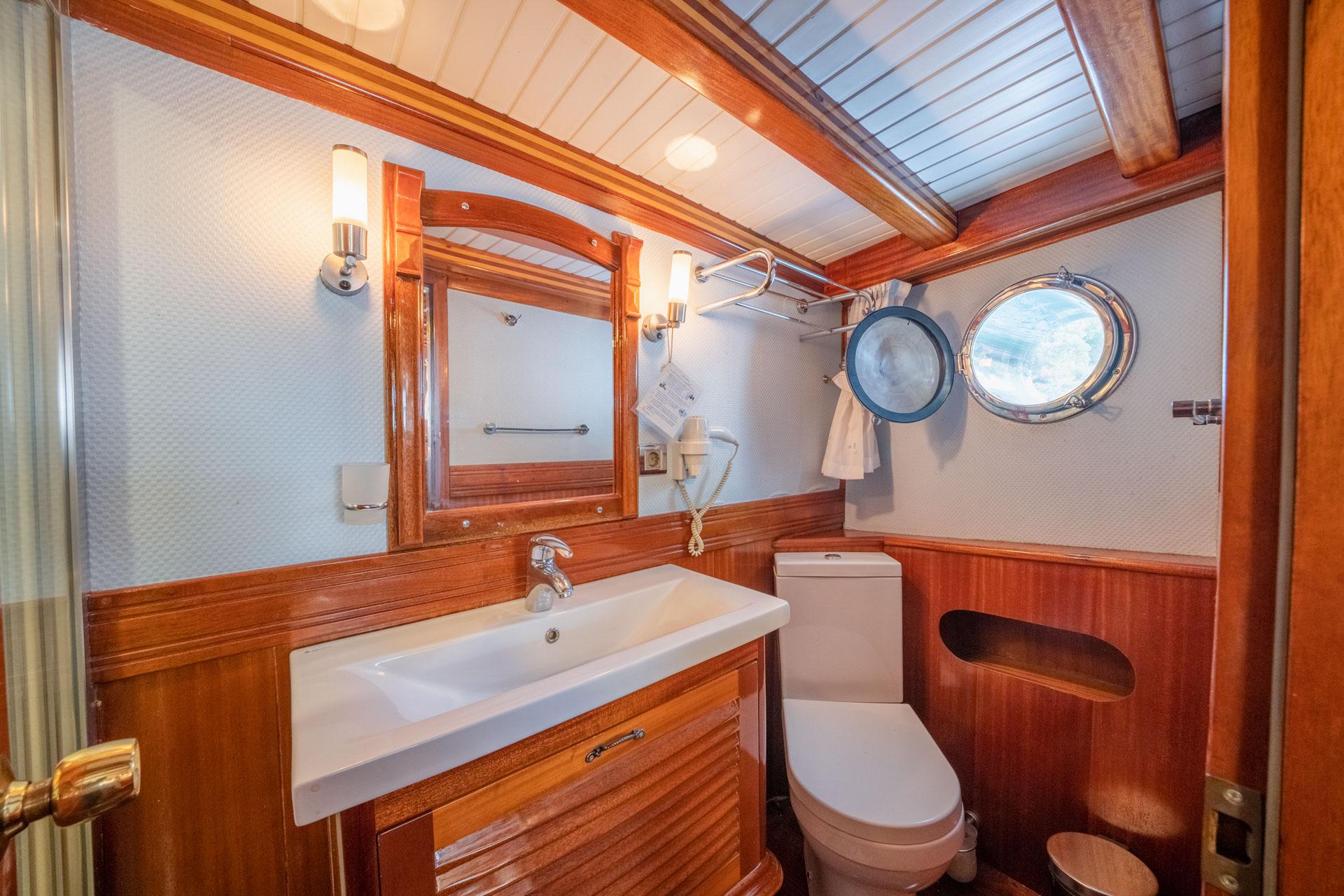 yacht bathroom featuring teak vanity, rectangular sink, mirror, toilet and two porthole windows