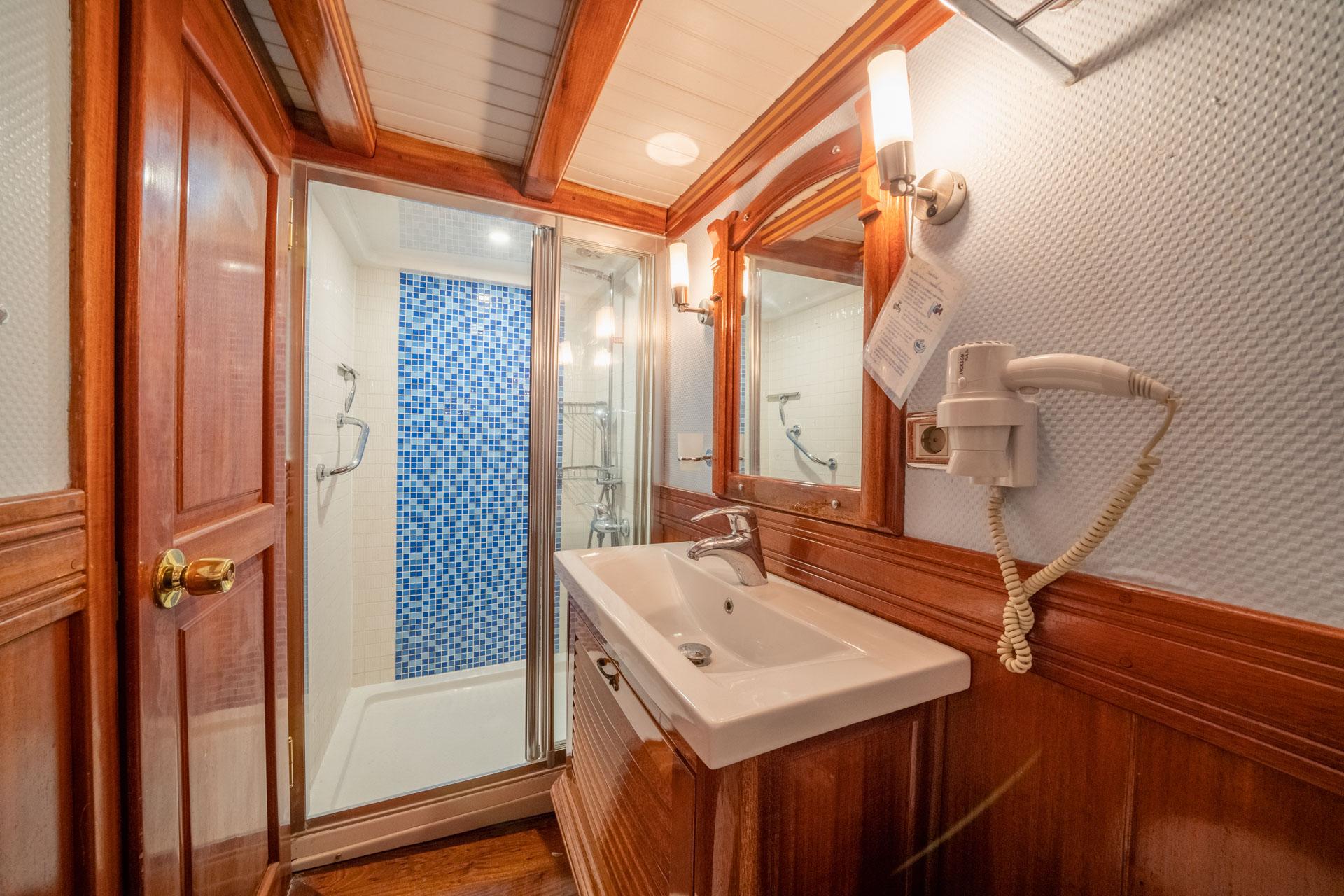 yacht bathroom featuring glass shower with blue mosaic tiles, white sink and rich wood cabinetry
