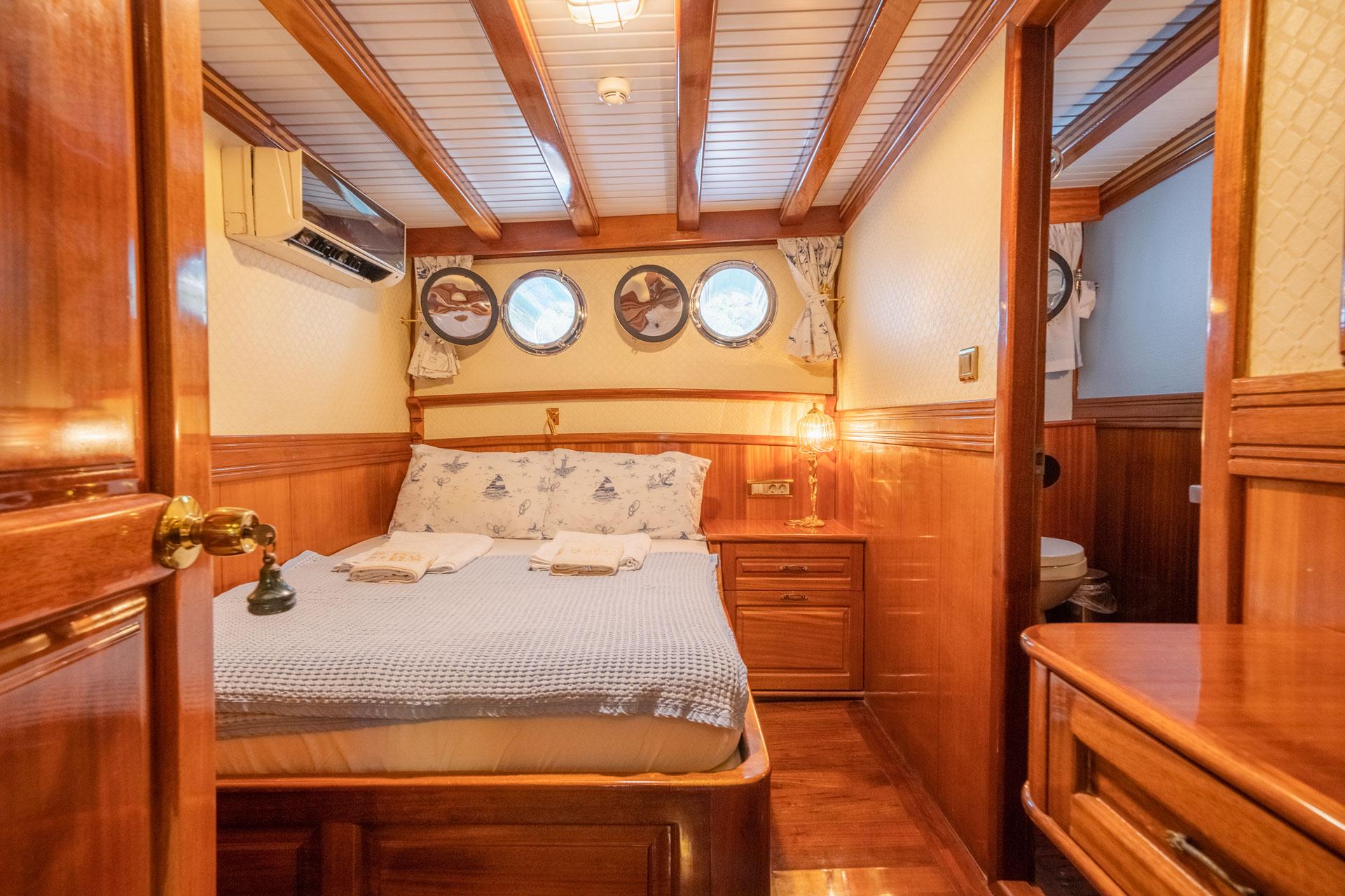 yacht guest cabin with double bed, wooden paneling, four portholes and en-suite bathroom