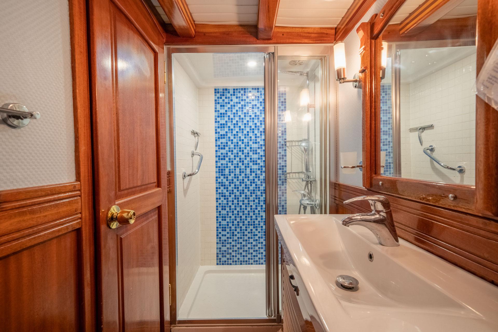 yacht bathroom featuring glass shower with blue mosaic tiles and rich wood paneling