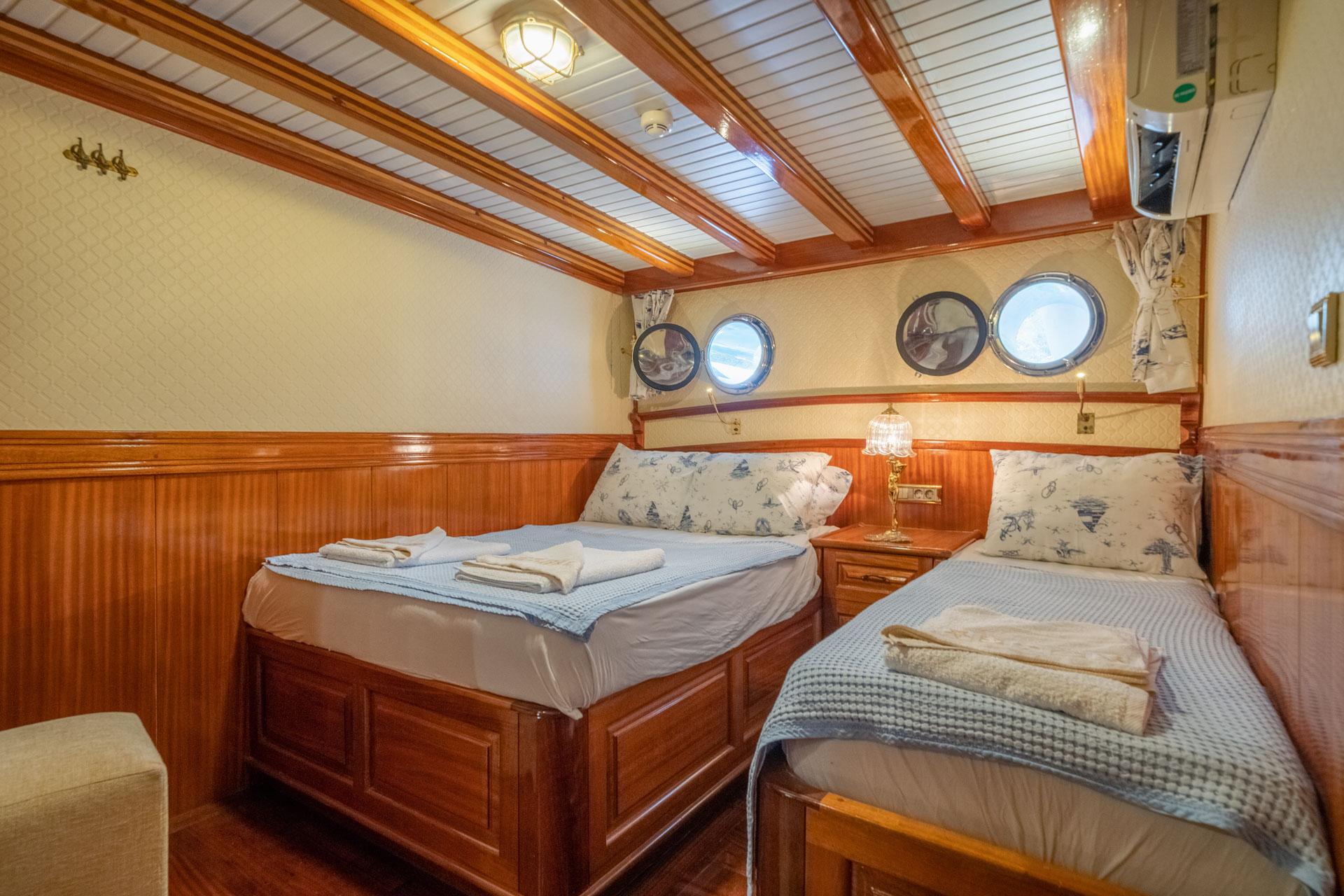 yacht twin cabin with two single beds, wooden paneling and round portholes