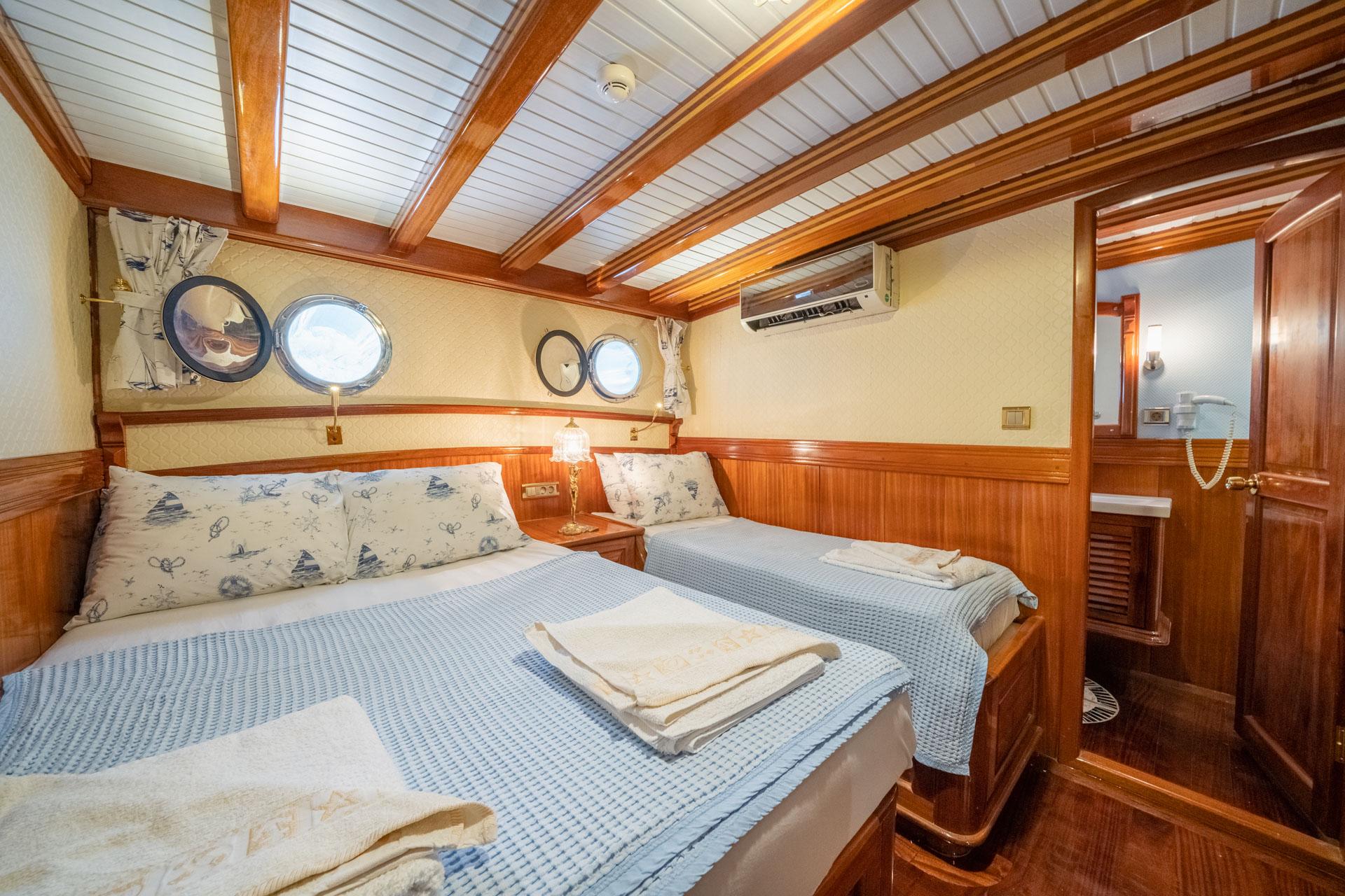guest cabin interior with twin beds, nautical bedding, wooden paneling and portholes