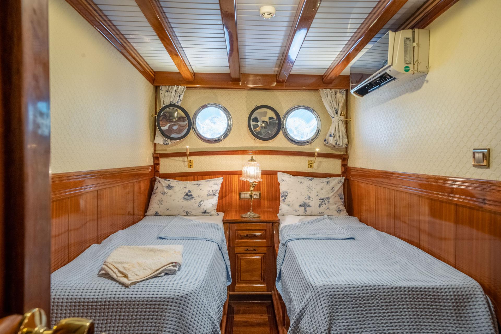 yacht twin bed cabin with two single beds, four portholes, wooden paneling and nautical decor