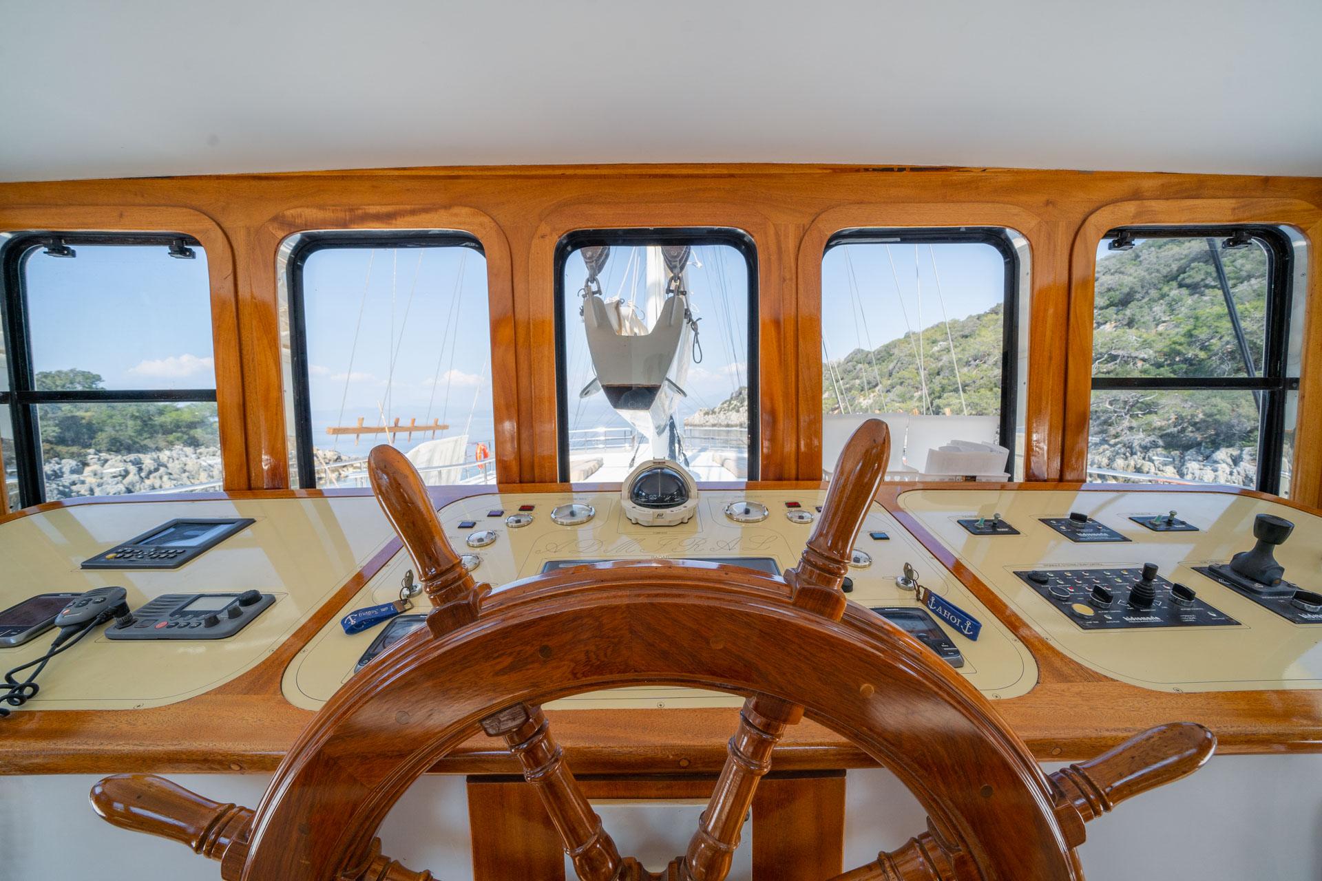 yacht helm station with wooden steering wheel and navigation instruments overlooking coastline