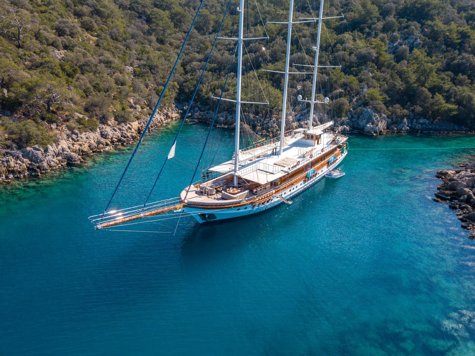 aerial view of traditional wooden gulet yacht anchored in crystal clear turquoise bay surrounded by forested coastline