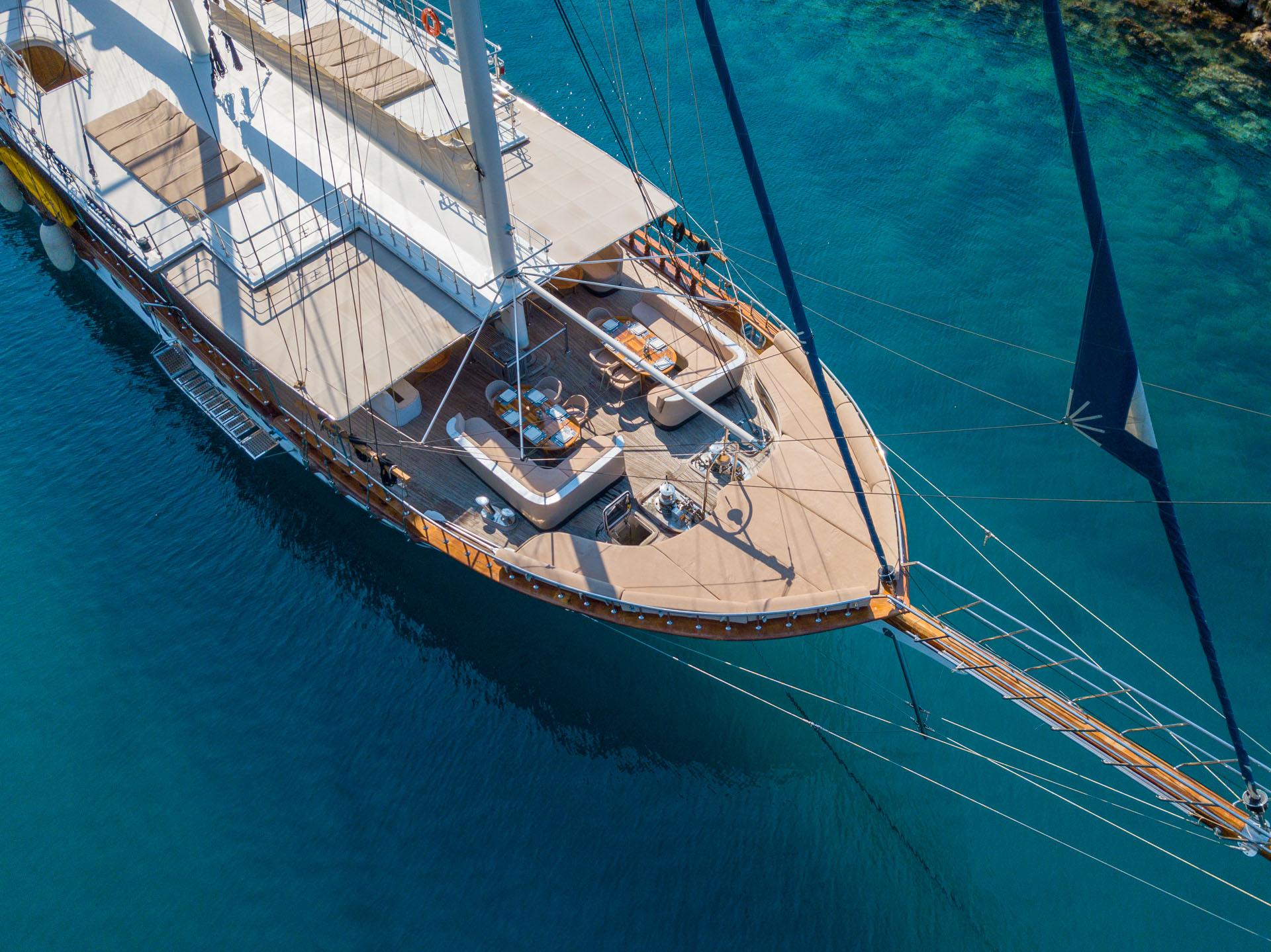aerial drone view of white gulet with wooden decks anchored in crystal clear turquoise waters