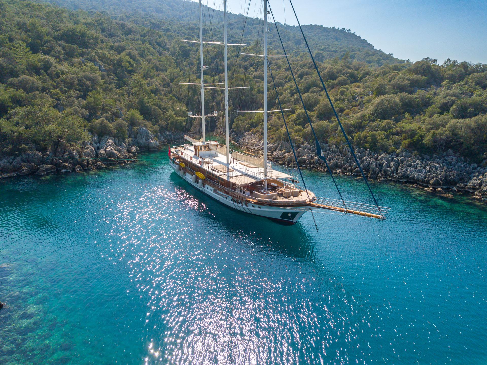 aerial view of traditional gulet yacht anchored in crystal clear turquoise bay surrounded by forested hills