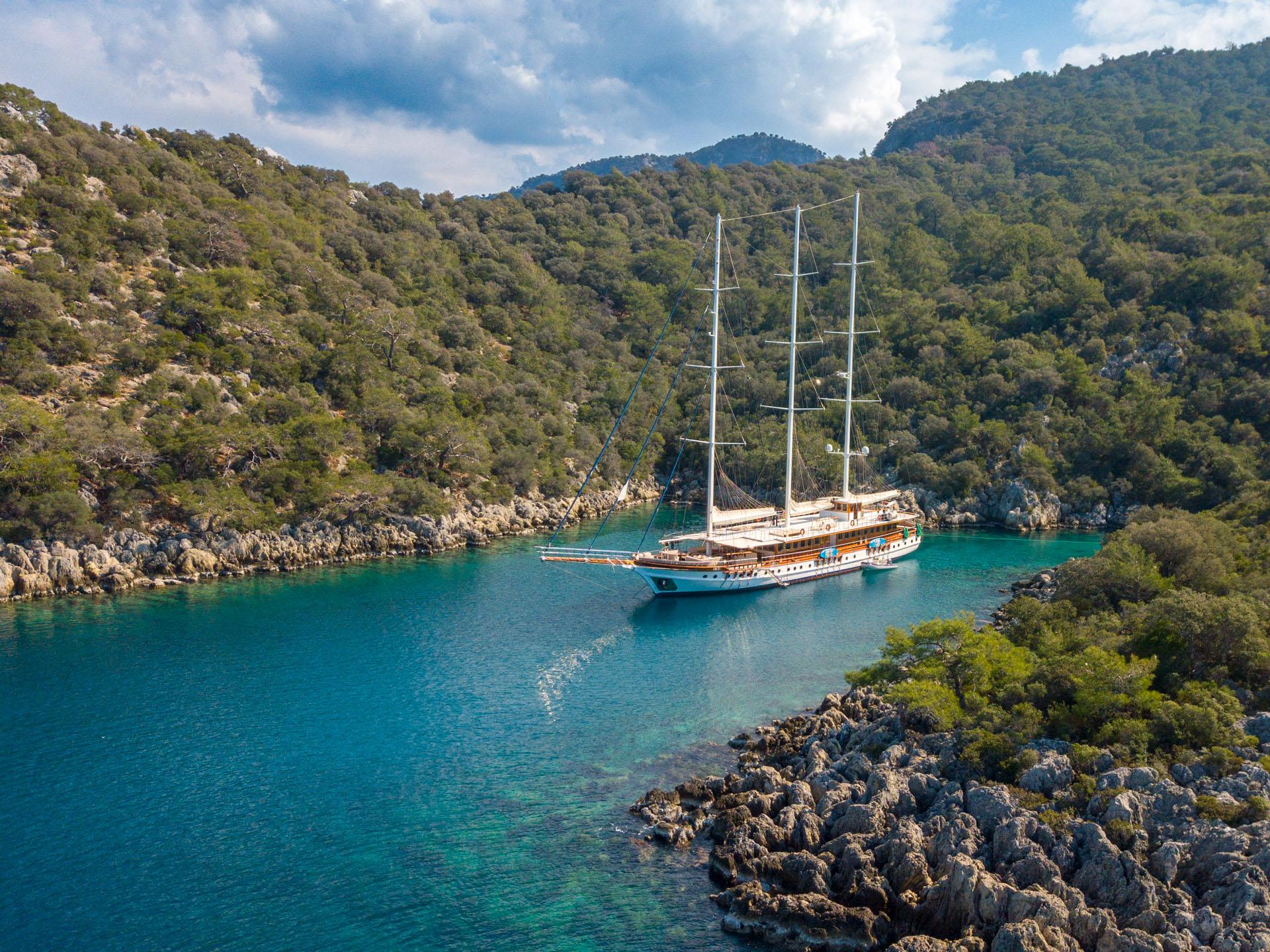 aerial view of traditional wooden gulet yacht anchored in crystal clear turquoise bay with forested hills