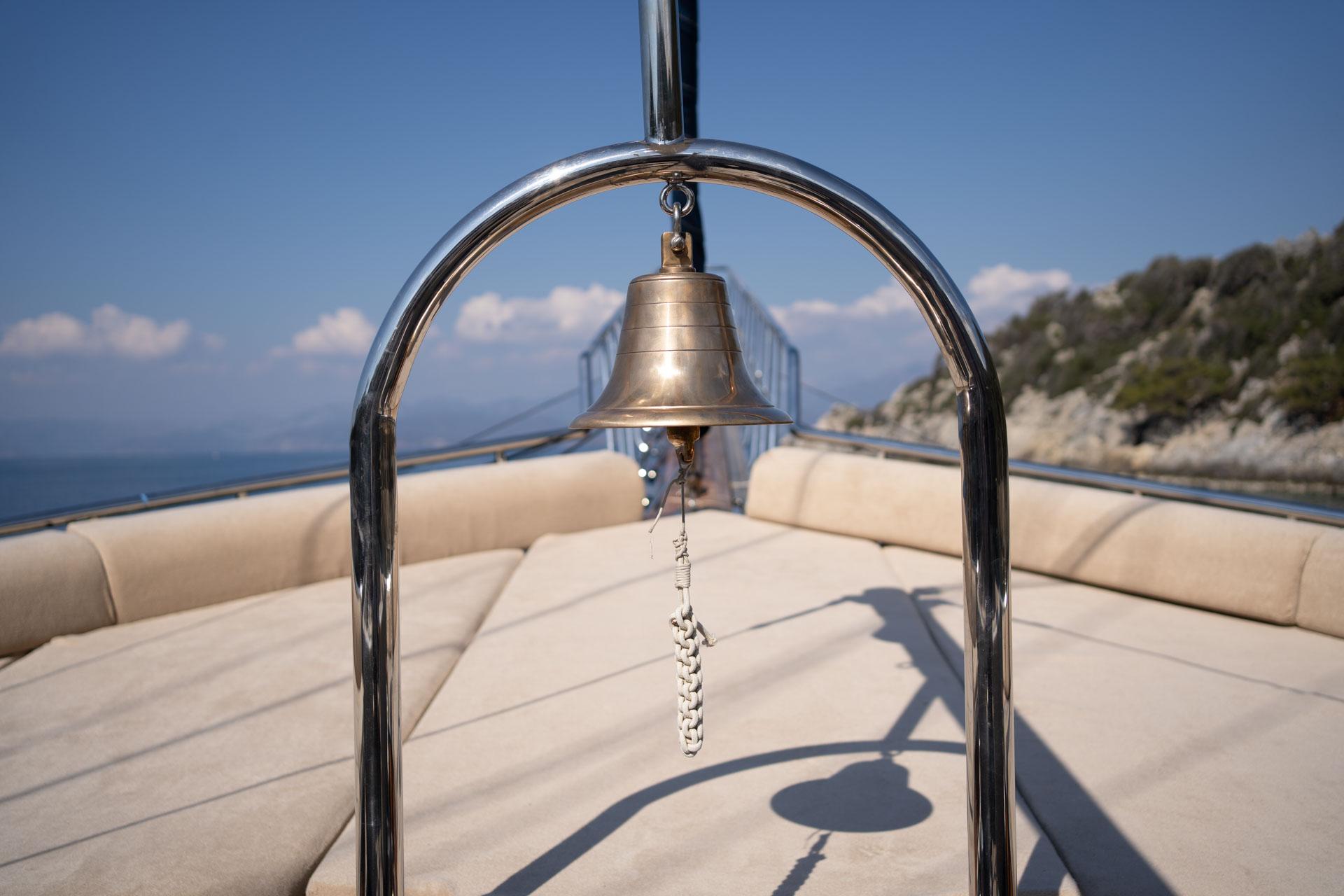 polished brass ship's bell on chrome stand with beige deck cushions and Mediterranean coastline