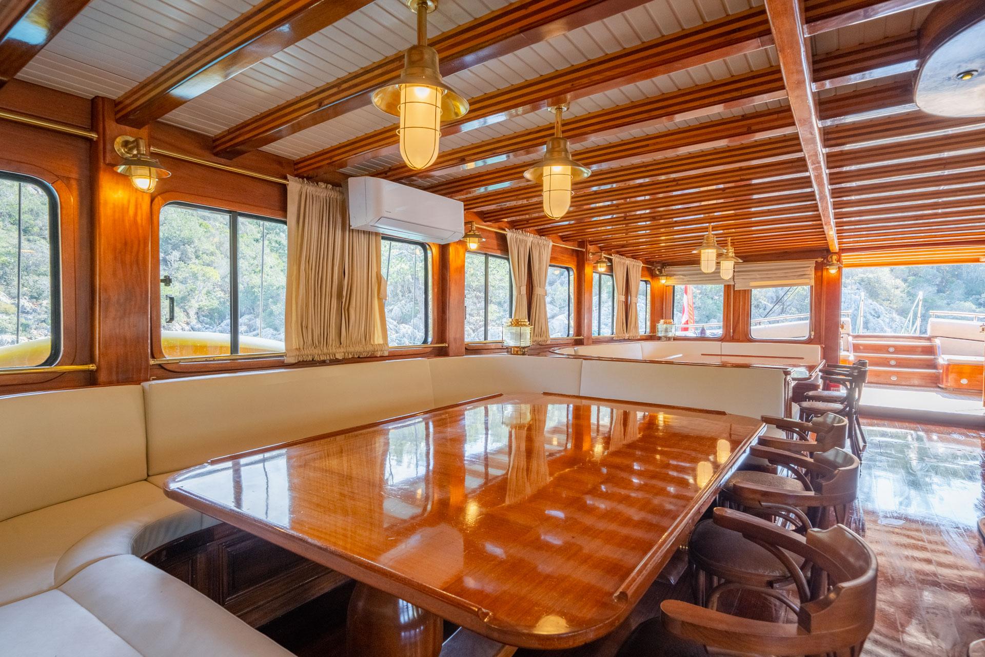 gulet indoor dining salon with glossy wood table, cream banquette seating and nautical pendant lighting