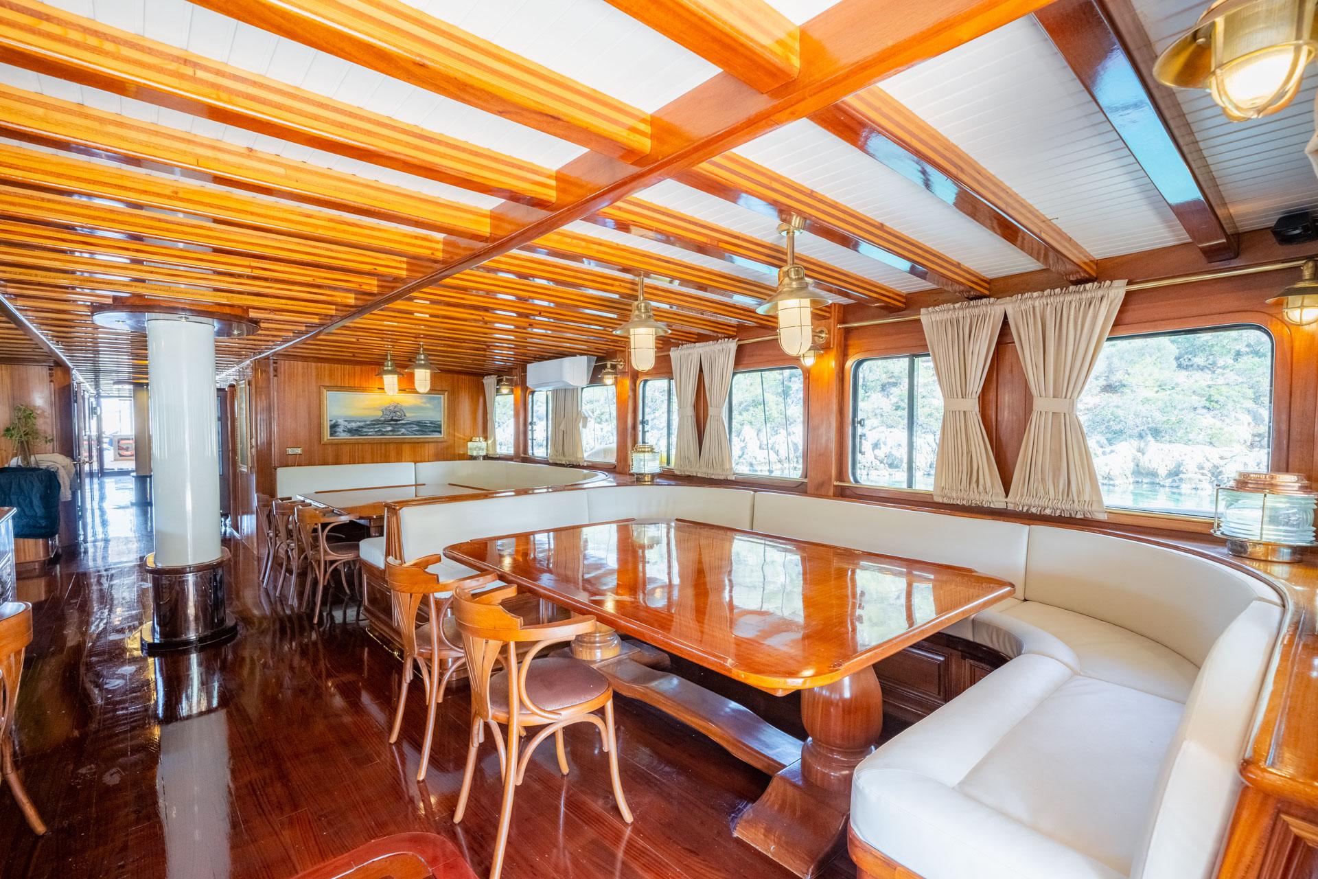 yacht interior salon with polished wood dining table, built-in banquette seating and exposed beam ceiling