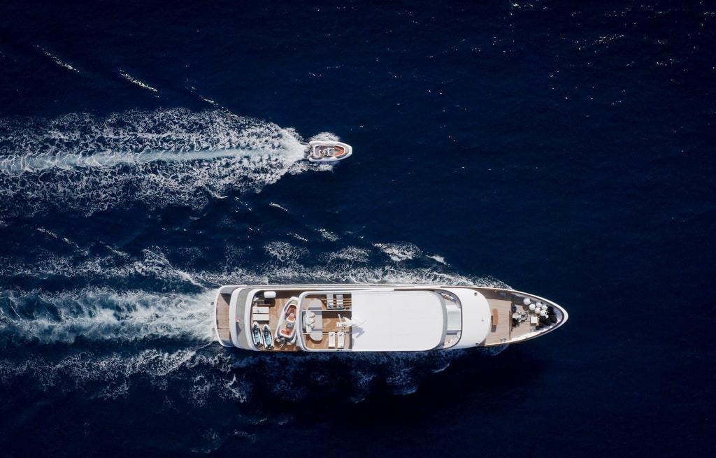 aerial view luxury motor yacht with tender boat creating wakes on blue water