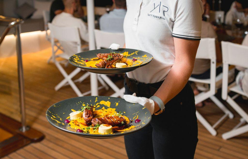 yacht crew serving elegant plated dishes with artistic yellow sauce presentation