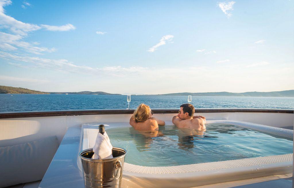 couple relaxing in yacht jacuzzi with champagne overlooking Mediterranean coastline