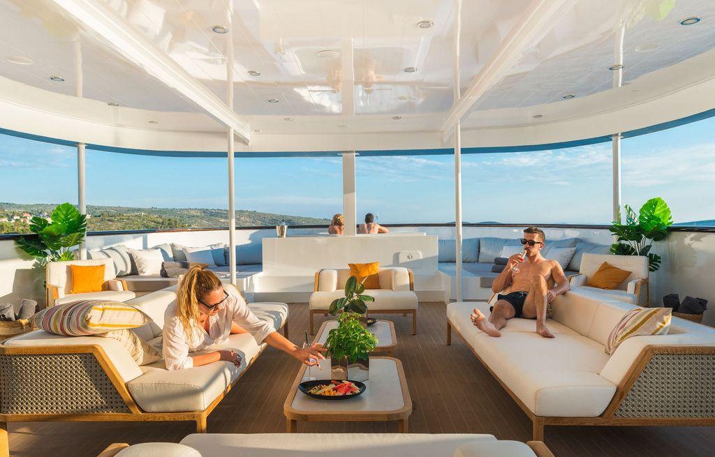 luxury yacht main deck salon with curved glass ceiling and guests lounging