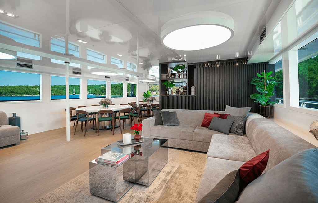 Modern yacht salon with gray sectional sofa, dining area, and panoramic water views