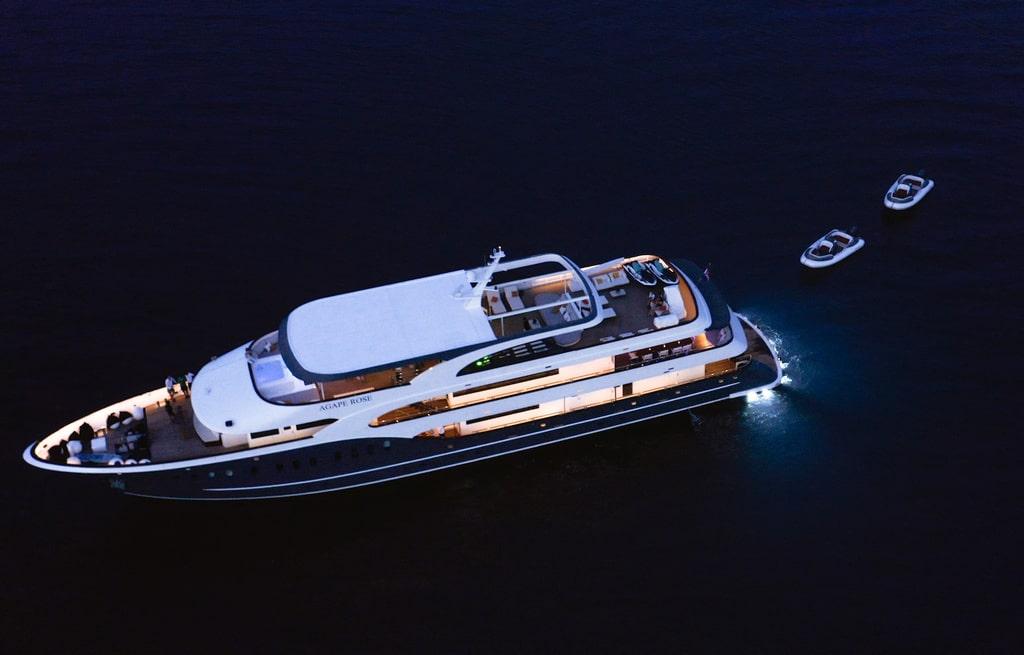 Aerial night view of illuminated white luxury motor yacht with two tenders