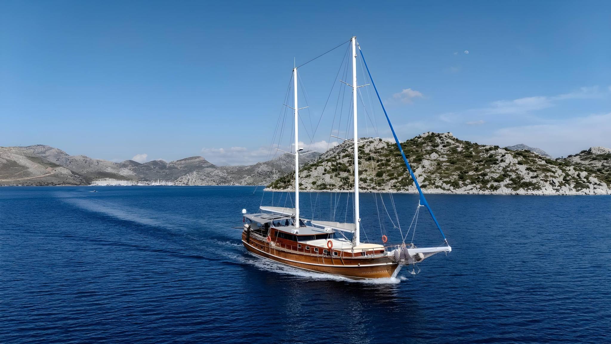 Traditional wooden gulet with two white masts sailing in deep blue Mediterranean bay surrounded by rocky hills