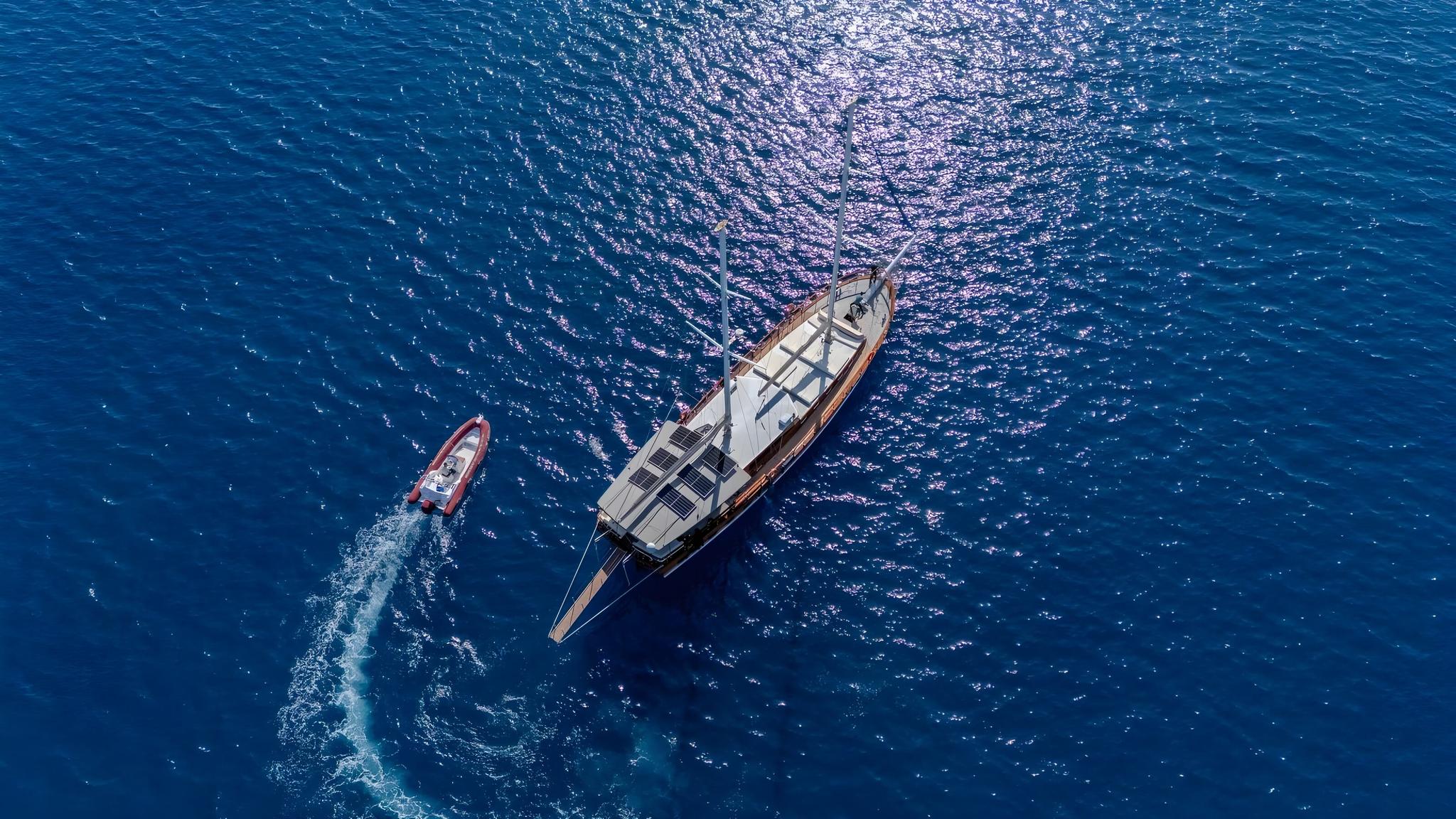 aerial view of traditional gulet yacht anchored with red tender boat creating wake trail