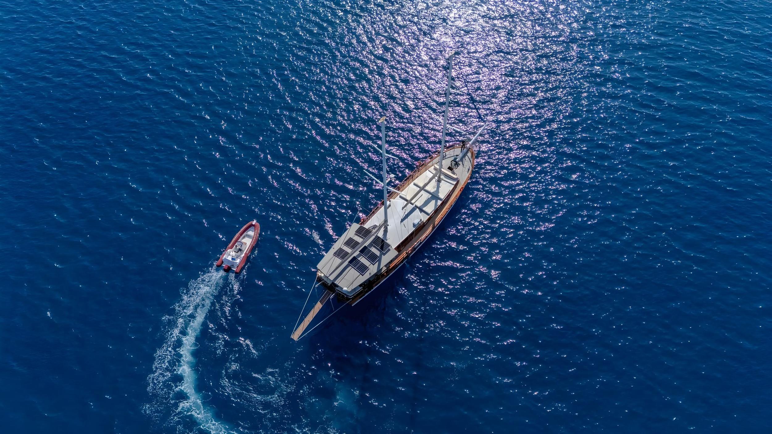 aerial view of traditional gulet yacht anchored with red tender boat creating wake trail