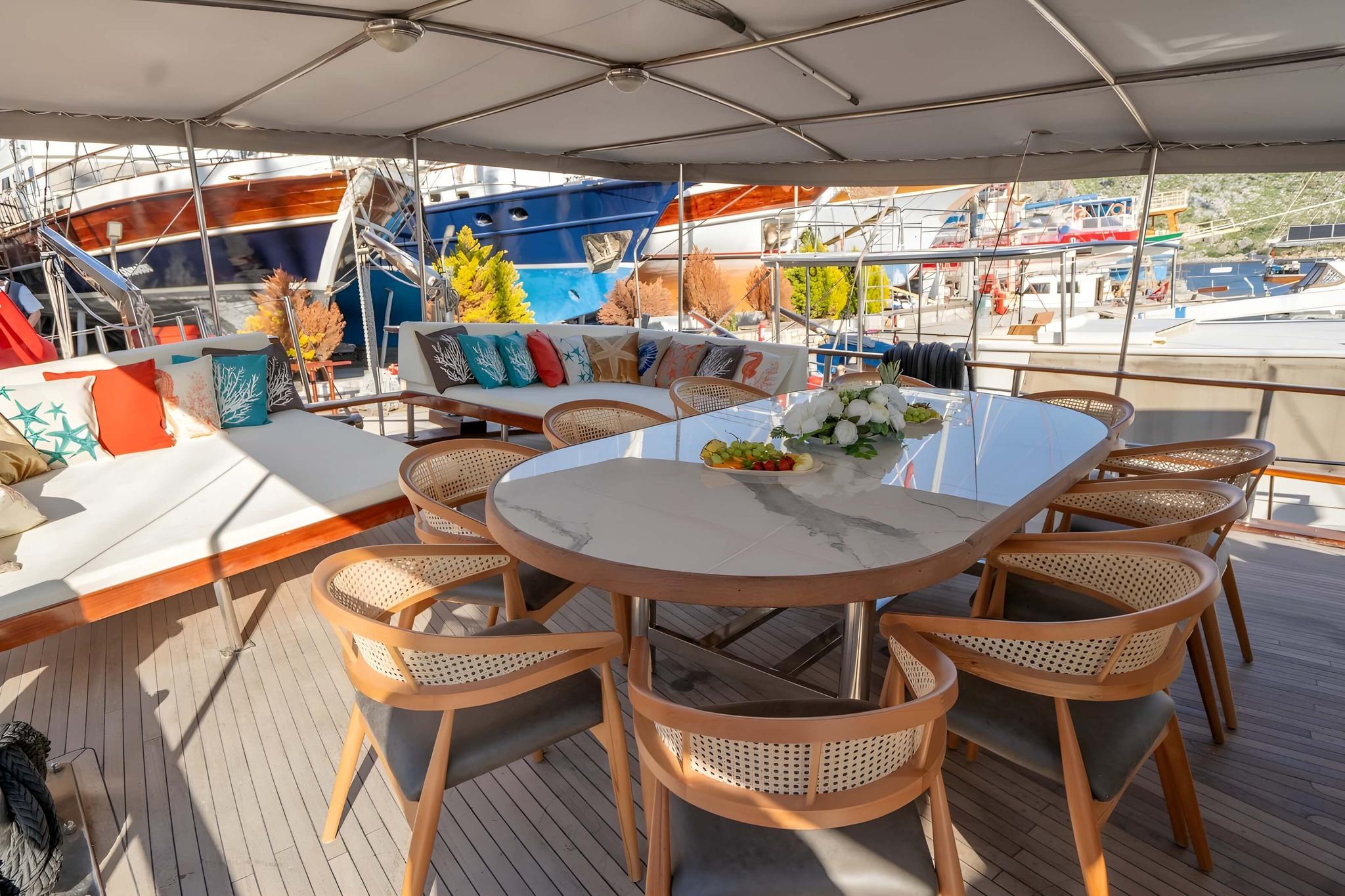 yacht aft deck with oval dining table, wicker chairs and seating area under canopy
