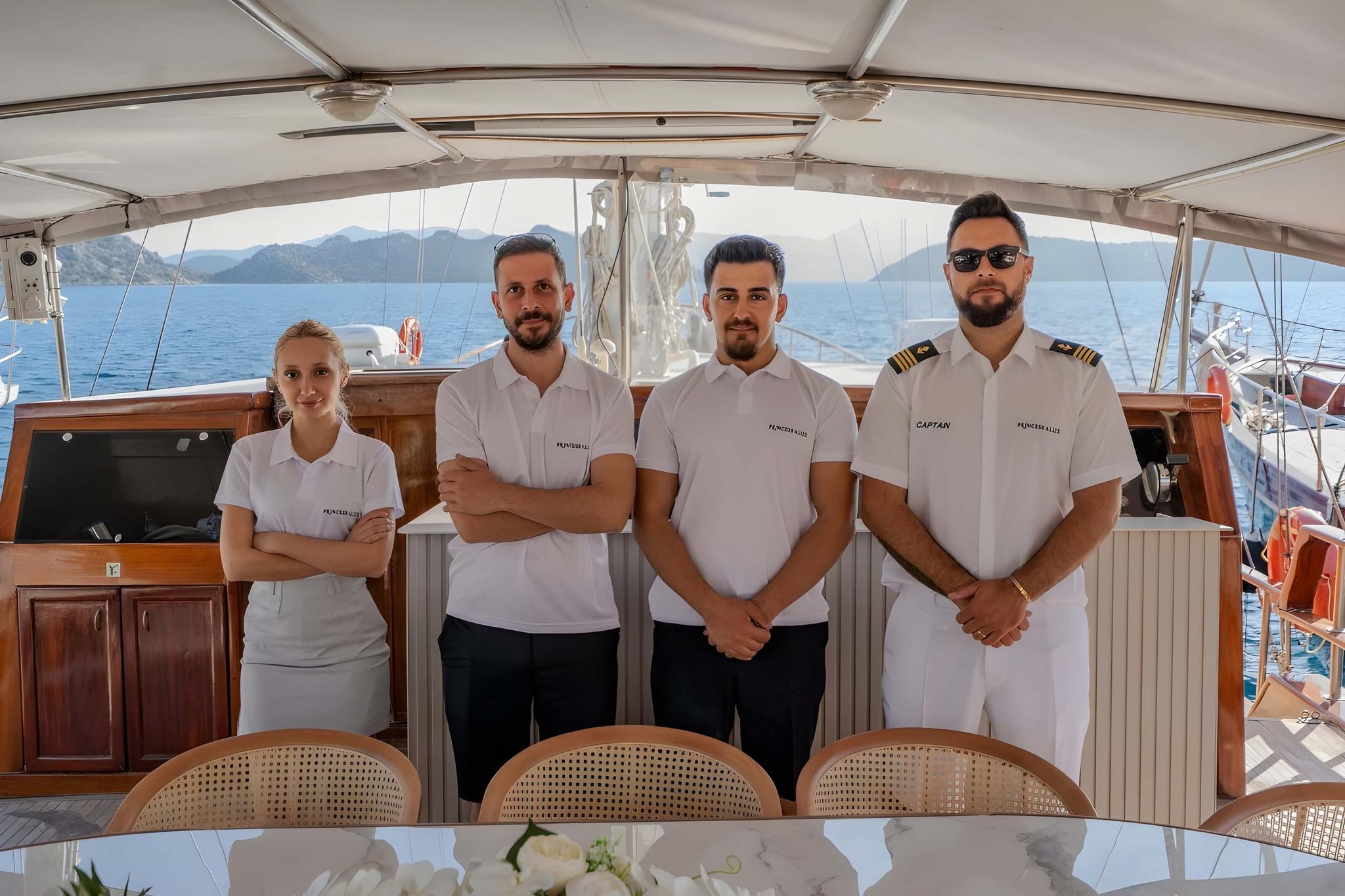four yacht crew members in white uniforms standing on aft deck with dining table
