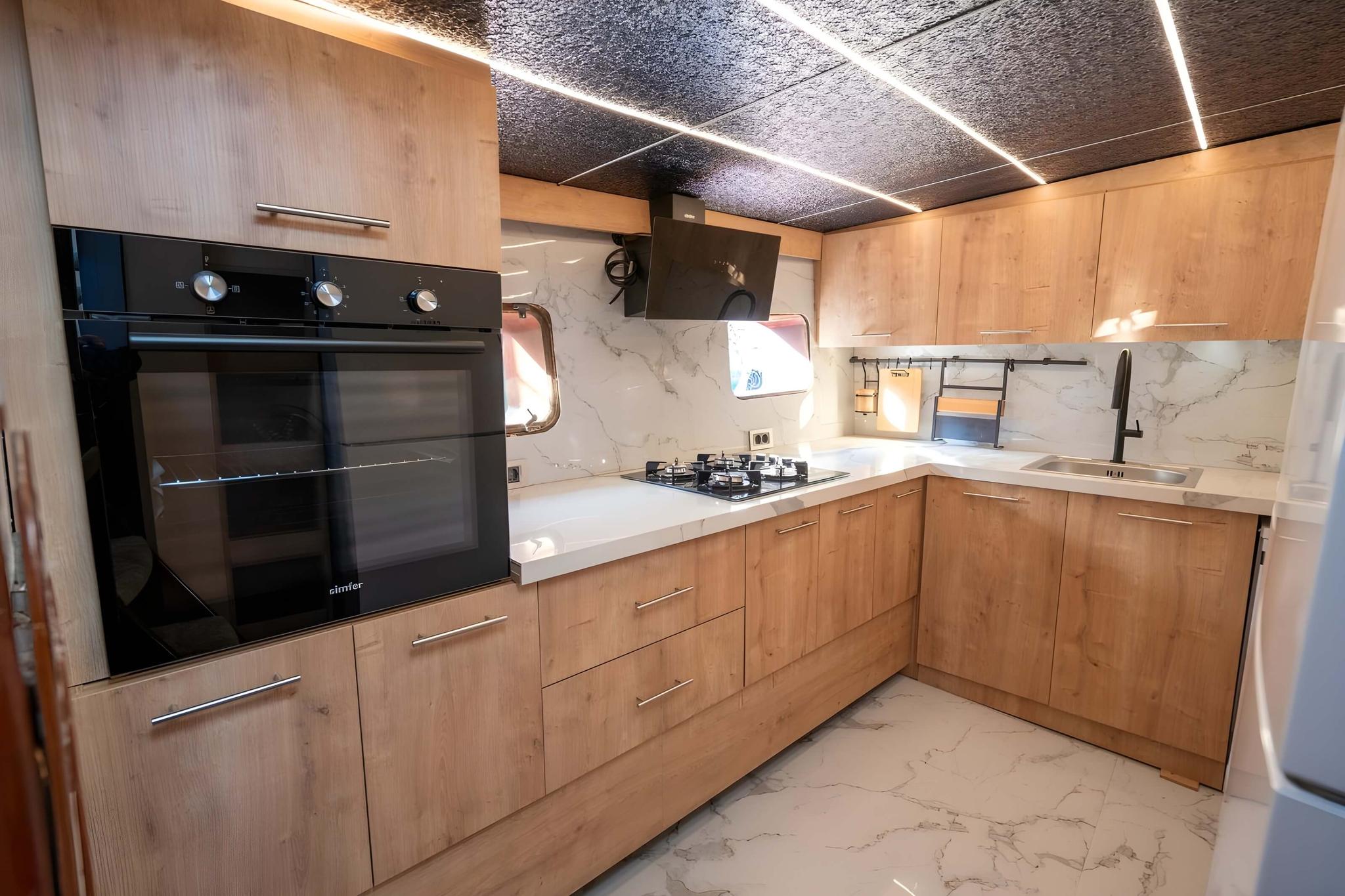 yacht galley featuring light wood cabinets, built-in oven, gas cooktop and white marble countertops