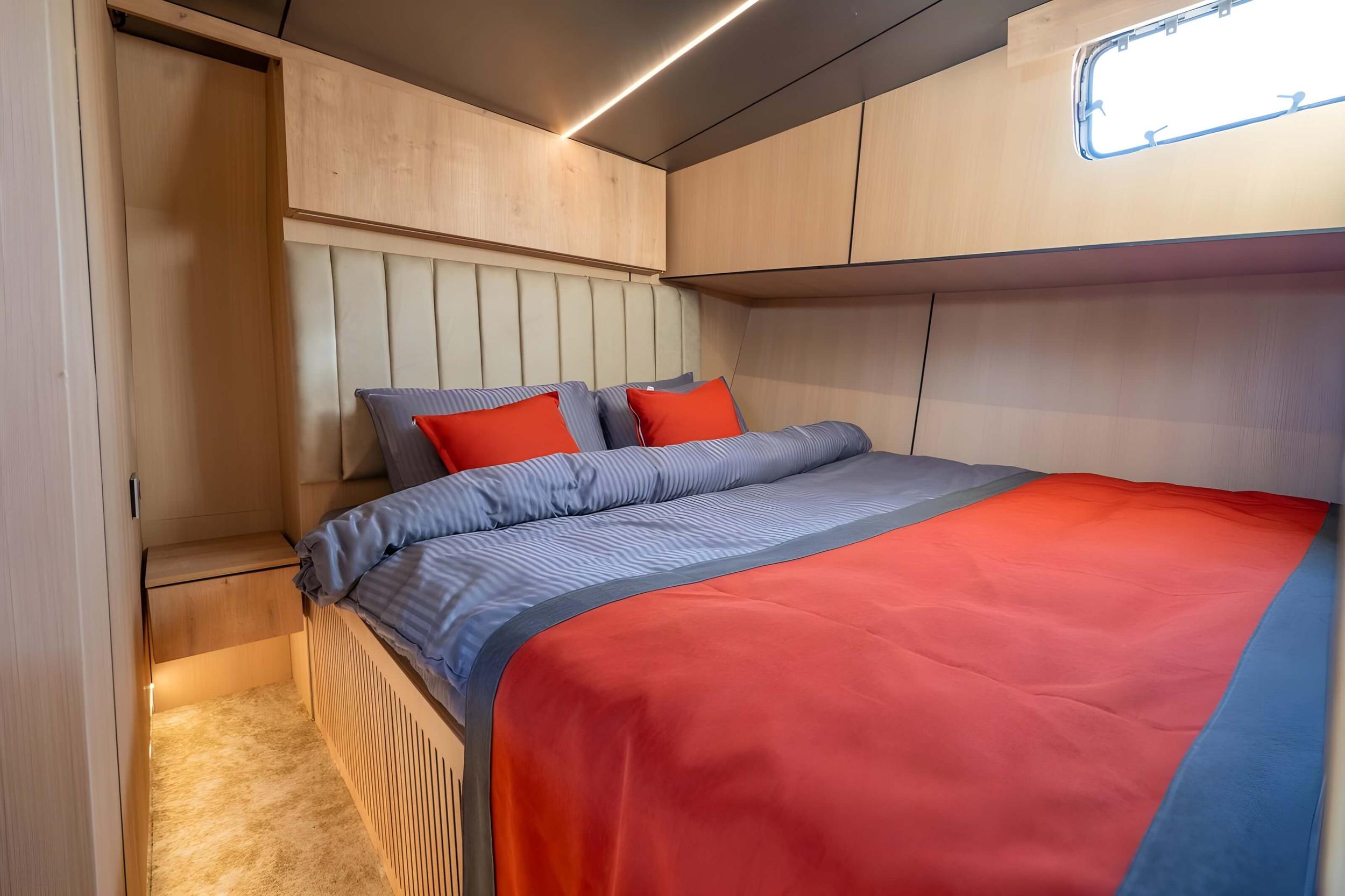yacht cabin interior with double bed, white upholstered headboard, red and blue bedding