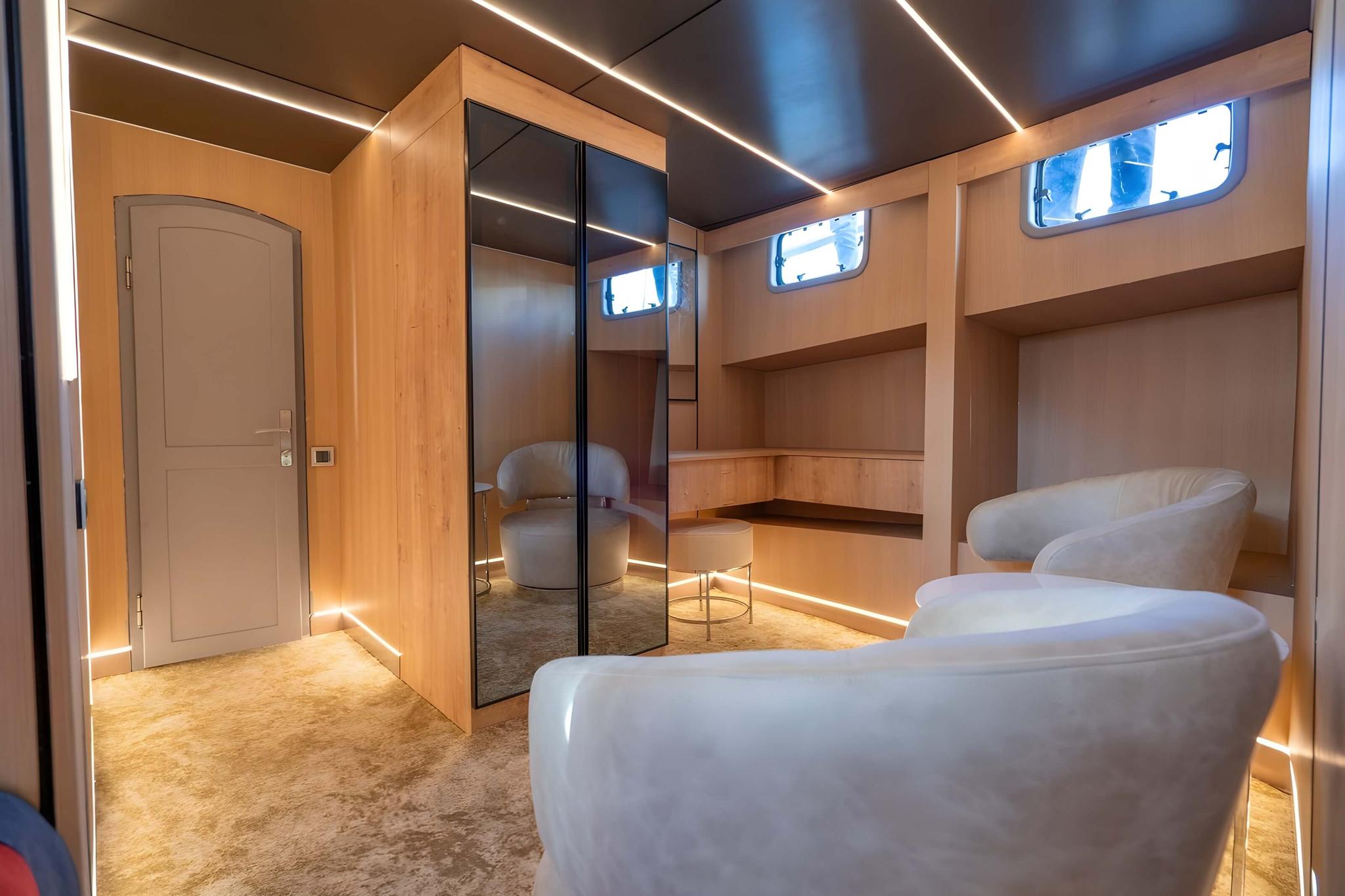 yacht cabin with curved white seating, built-in shelving, mirrored wardrobe doors and portholes