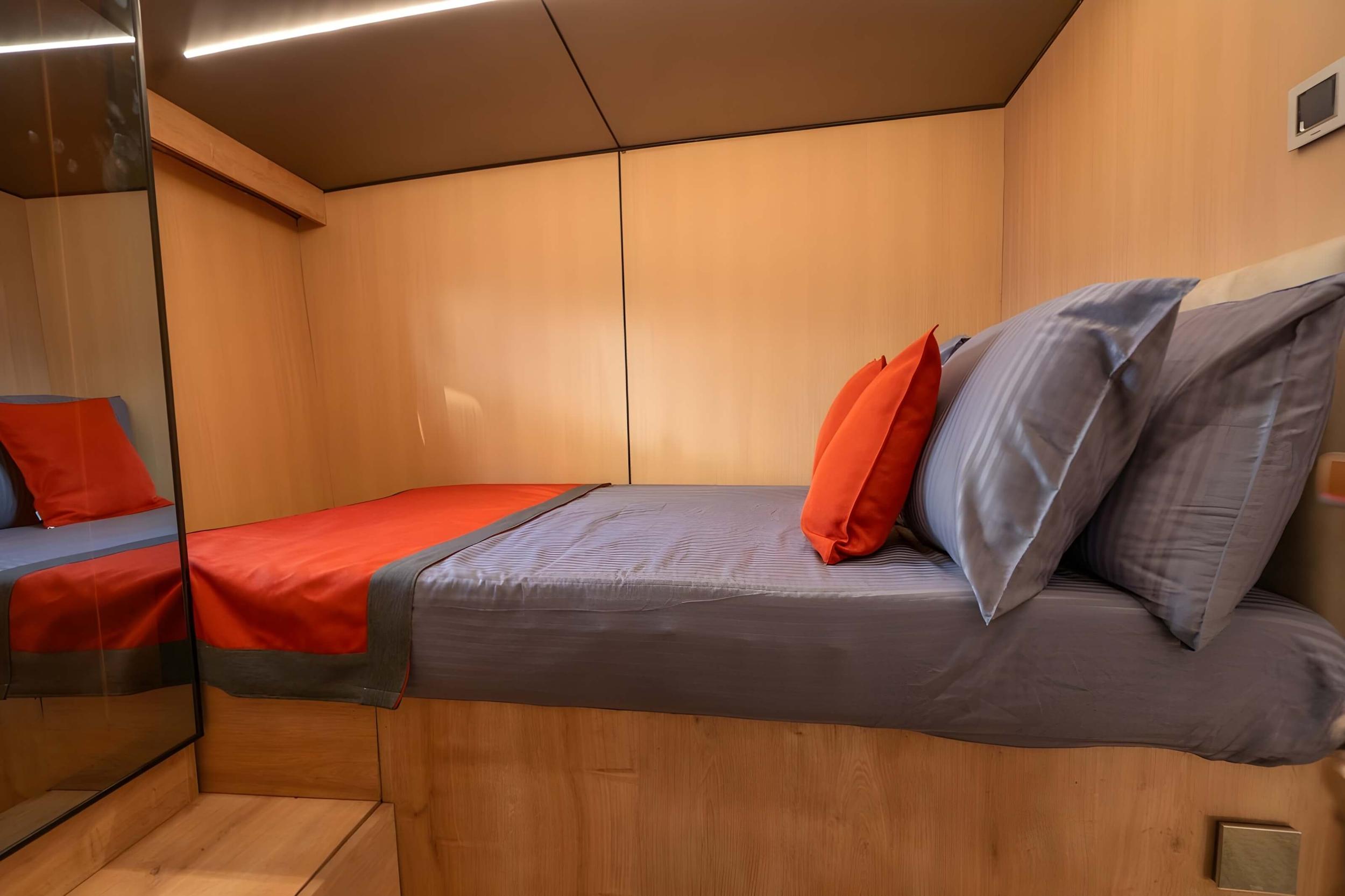 yacht guest cabin featuring twin beds with grey and orange bedding, light wood paneling