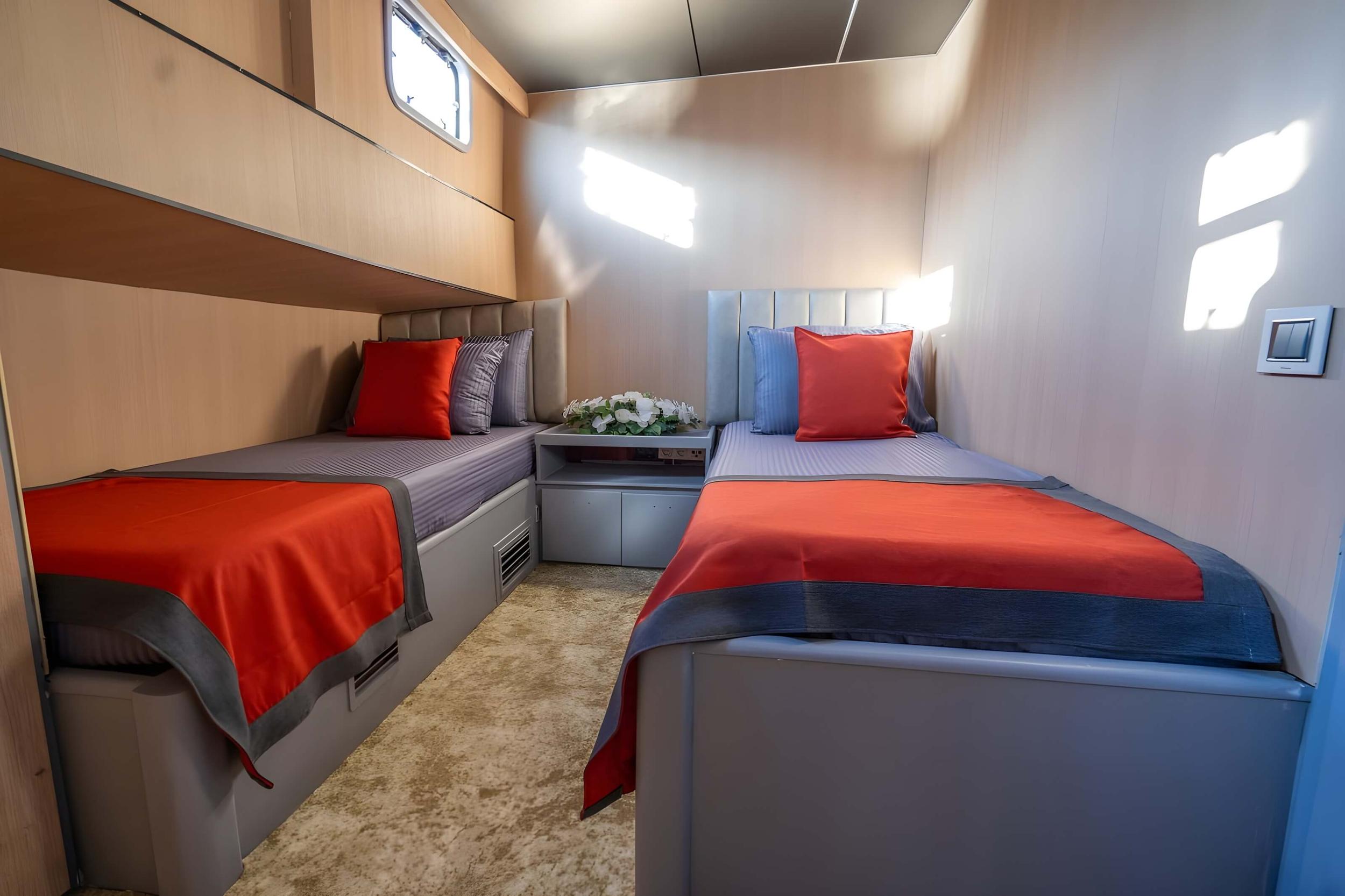 yacht twin cabin with two single beds, red throws, upholstered headboards and porthole window