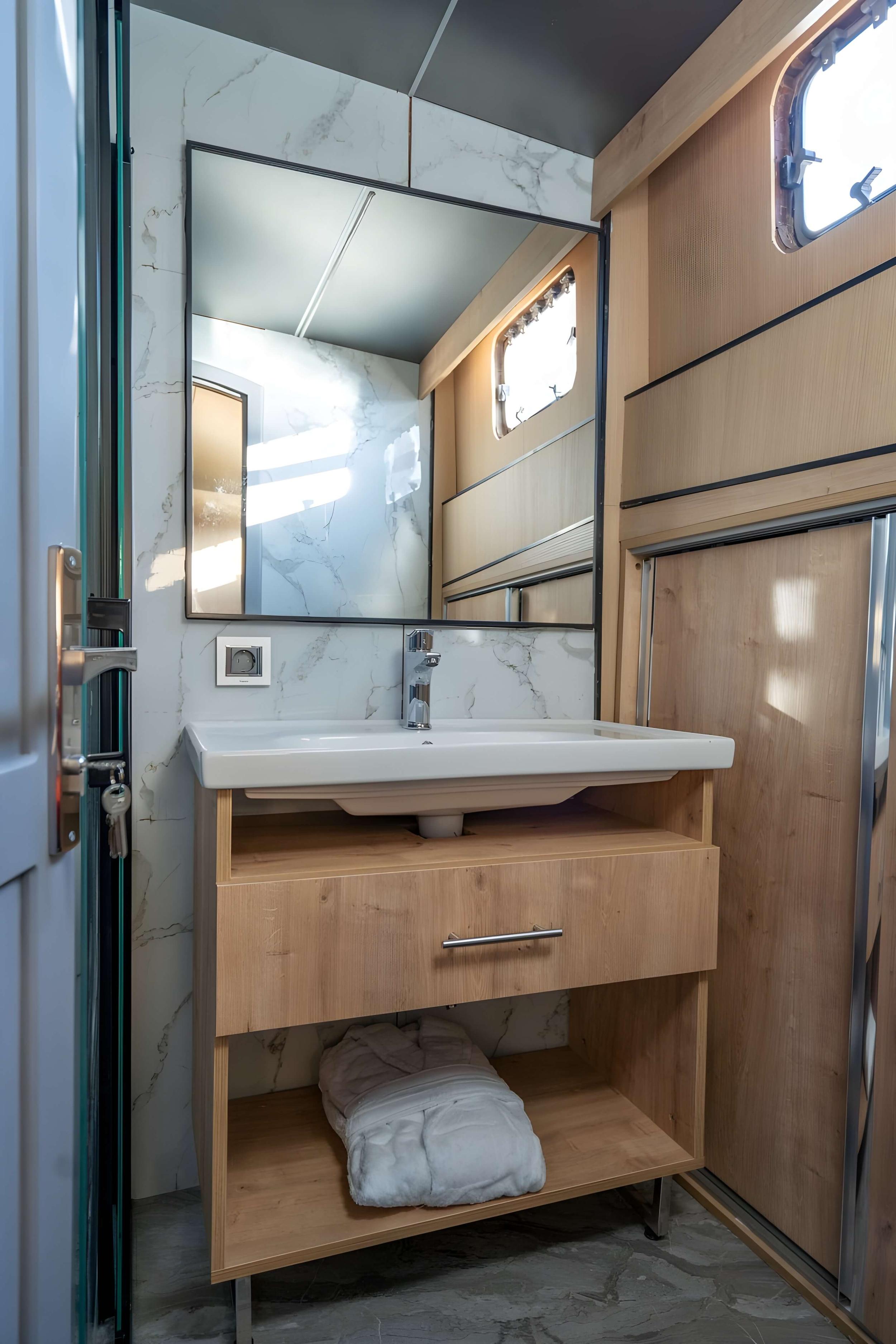 yacht bathroom with white vessel sink, marble walls, wooden storage vanity and porthole window