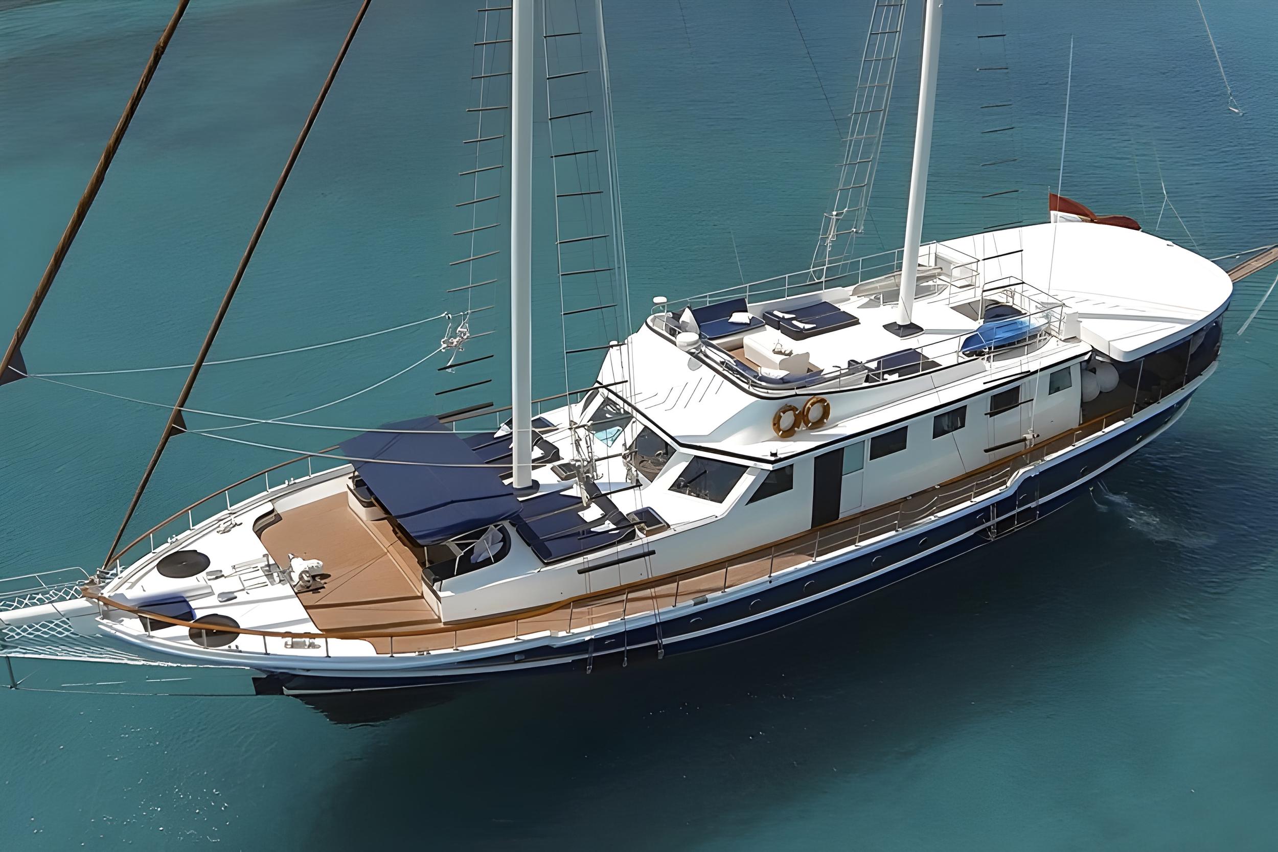 white motor sailing yacht with two masts anchored in clear turquoise Mediterranean waters